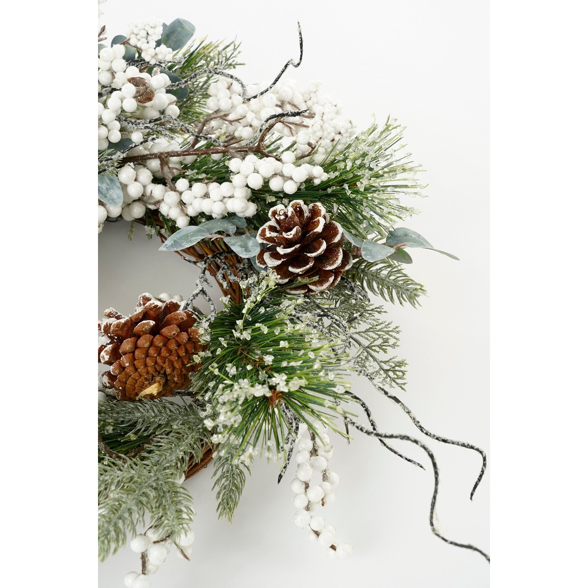 Winterlicher Weihnachtskranz mit Tannenzapfen, weißen Beeren und künstlichem Schnee auf weißem Hintergrund.