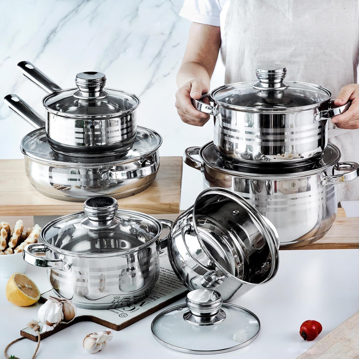 Una persona sostiene una olla de acero inoxidable entre un juego de utensilios de cocina.