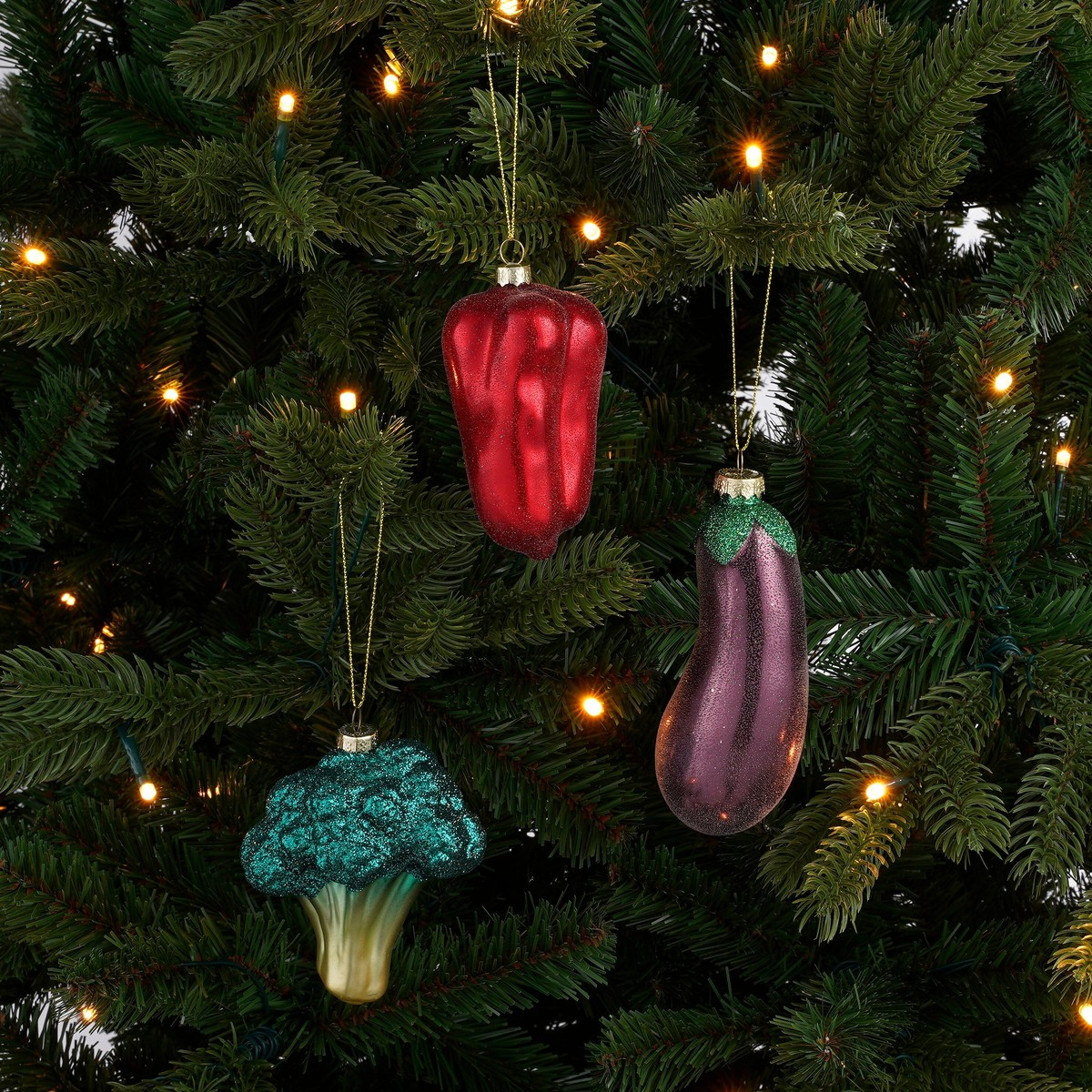 Gemüse-Weihnachtsbaumschmuck: rote Paprika, lila Aubergine und grüner Brokkoli an einem beleuchteten Tannenbaum.