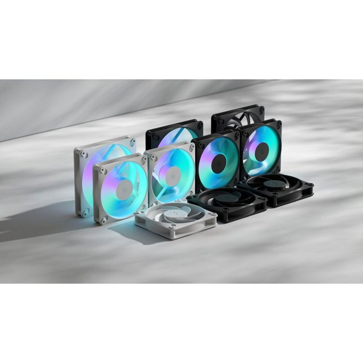 Mehrere schwarze und weiße PC-Lüfter mit RGB-Beleuchtung stehen auf einem hellen Untergrund in einem Raum.