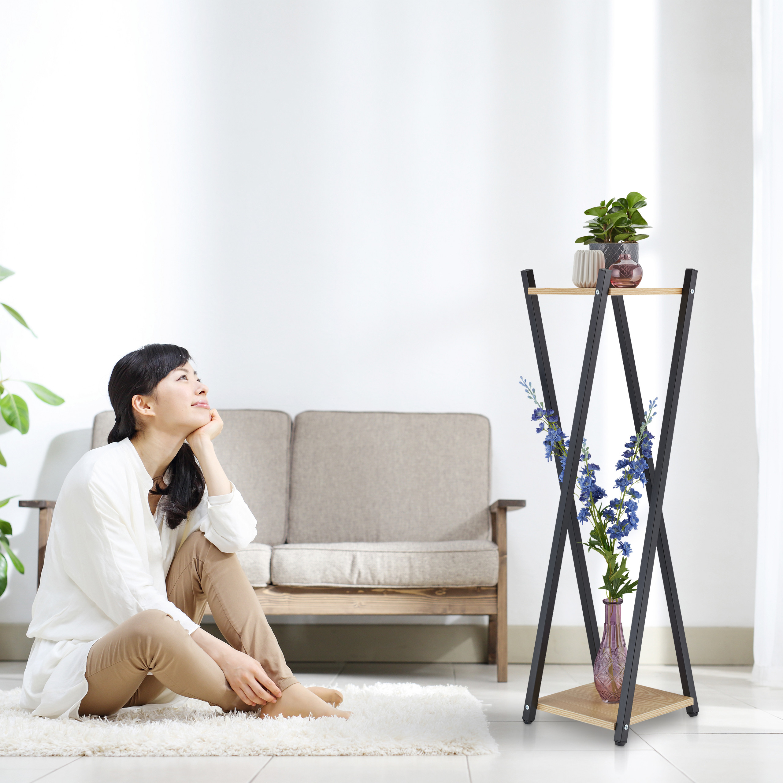 Eine sitzende Frau sieht eine moderne Blumenständer in einem hellen Wohnzimmer an.