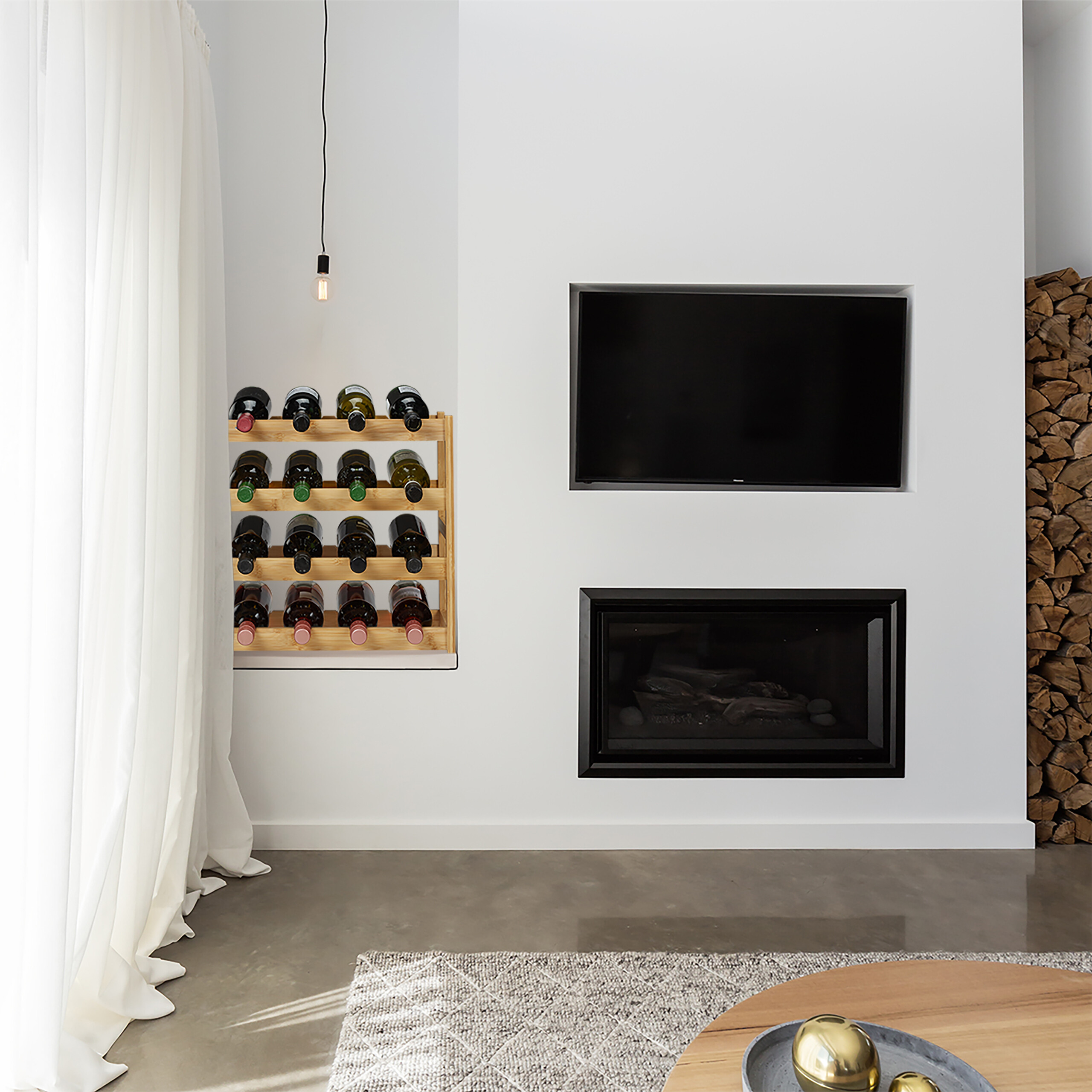 Moderne Wand mit TV, Kamin, Holzregal und Weinen, beleuchtet von einer Lampe.