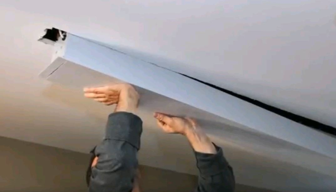 Persona che installa un lungo apparecchio bianco su un soffitto.