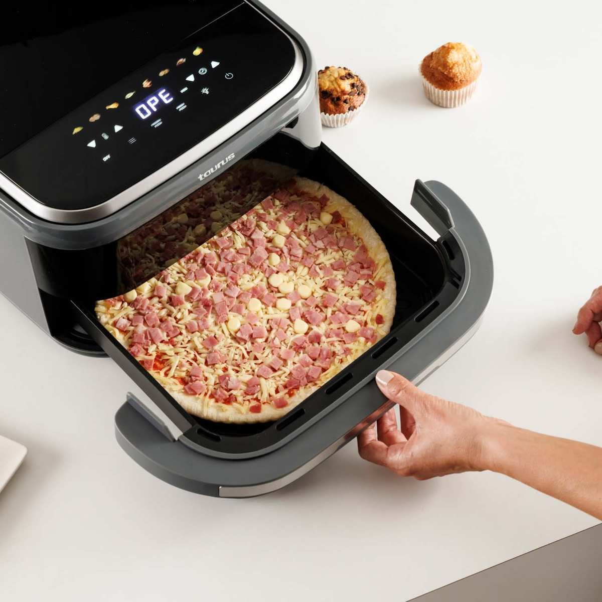 Una mano abre una cesta de freidora de aire que contiene una pizza cruda.
