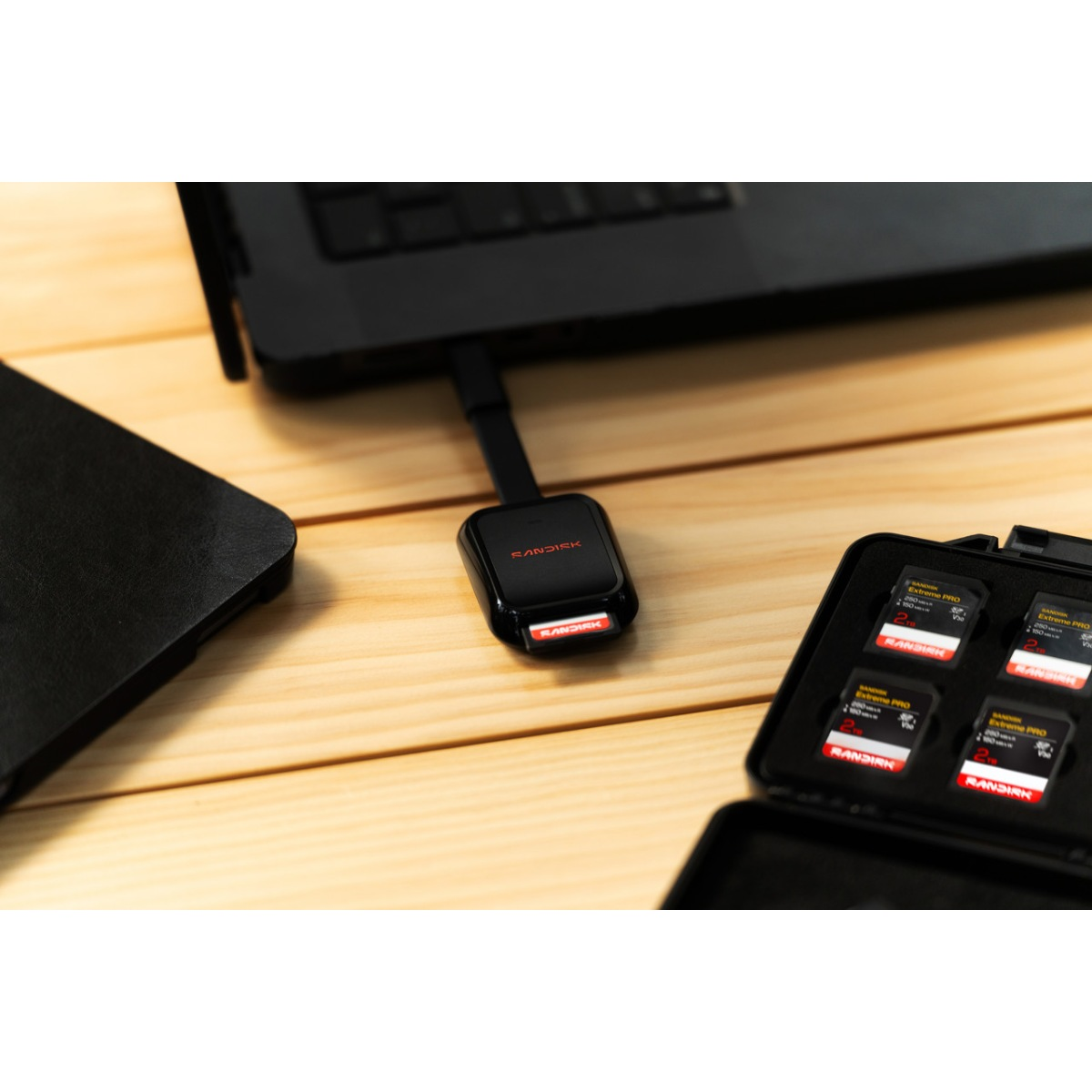 Un lecteur de carte SanDisk noir branché à un ordinateur portable, près d'un étui de cartes SD.