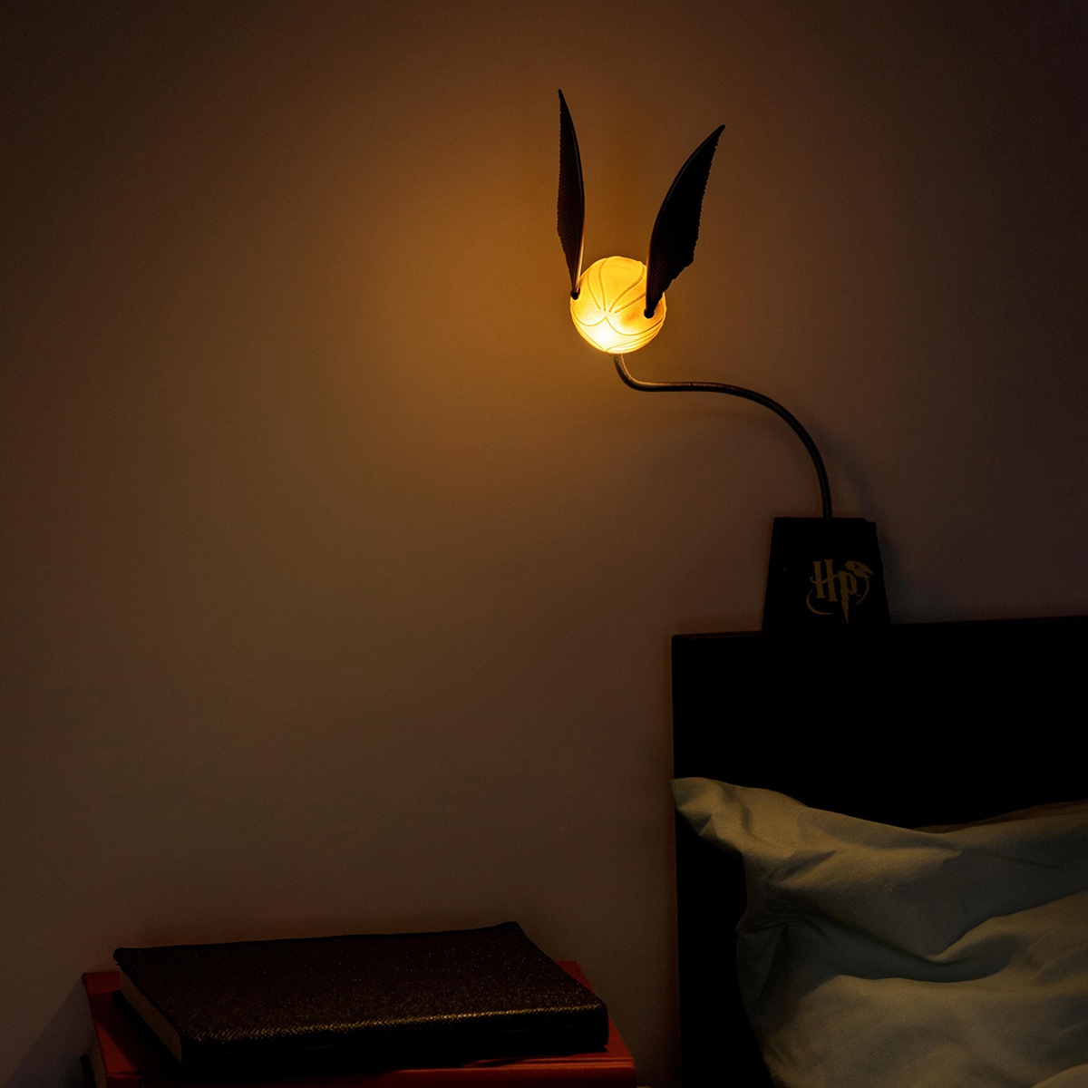 Una lámpara de la Snitch dorada está montada en la pared sobre una cama.