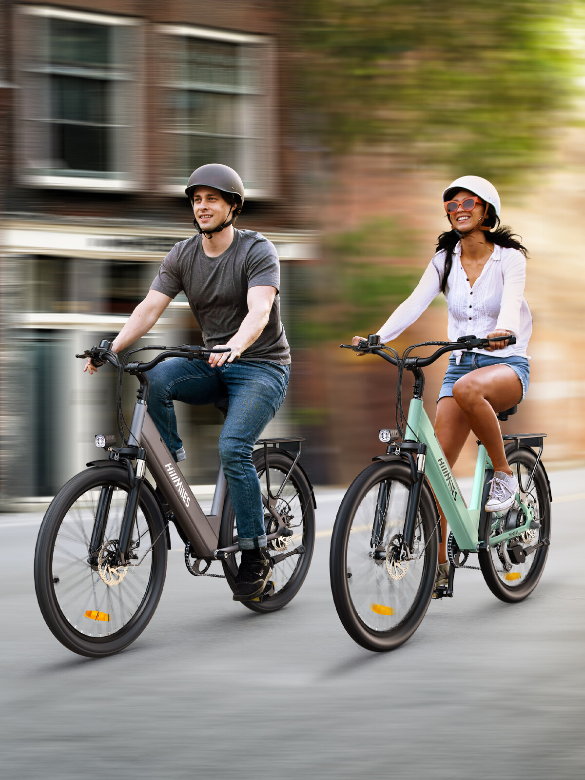 Ein lächelnder Mann und eine Frau fahren mit E-Bikes durch eine Straße, tragen Helme und Freizeitkleidung.