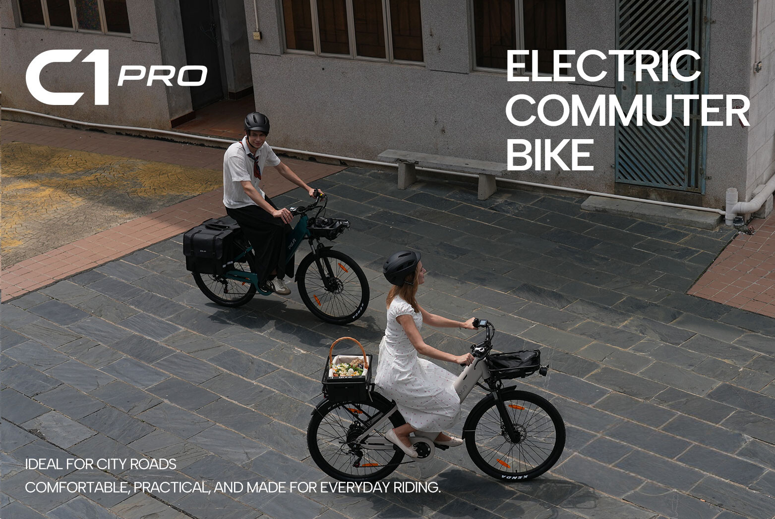 Due persone guidano biciclette elettriche da città su strade pavimentate grigie di fronte a un edificio.