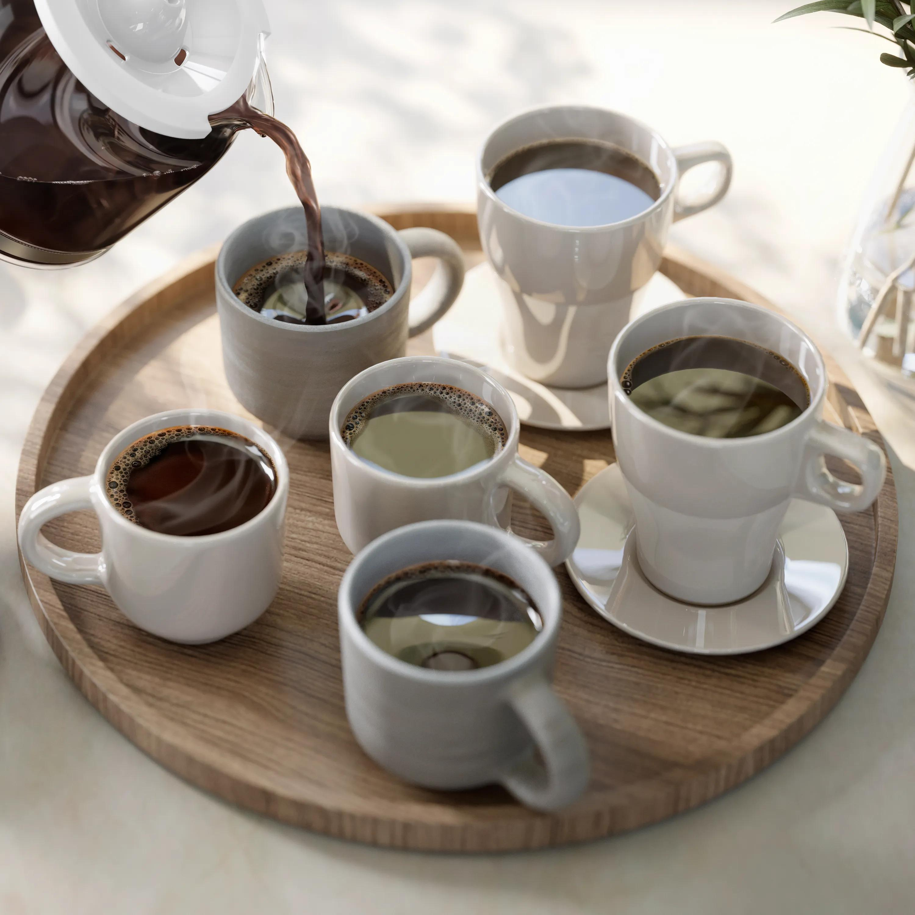 Se vierte café de una tetera en una taza en una bandeja de madera con otras tazas de café.