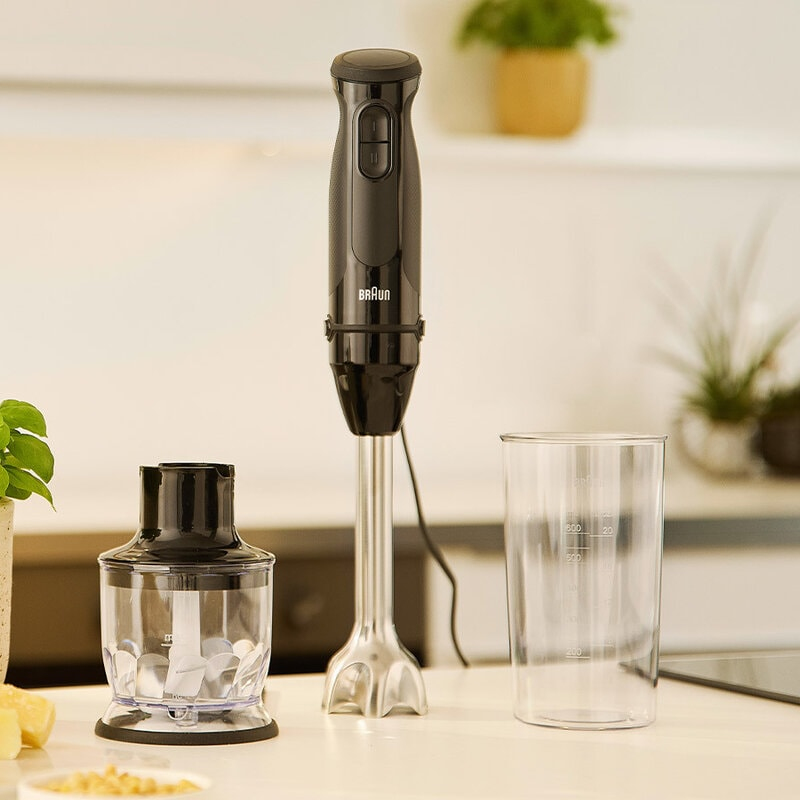 Siyah bir Braun el blenderi mutfak tezgahında duruyor, yanında bir doğrayıcı ve ölçü kabı var.