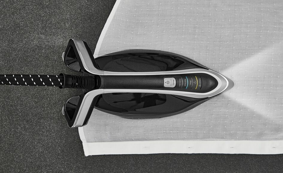 Un ferro da stiro nero stira tessuto bianco su una superficie grigia, con luce LED integrata sulla punta.