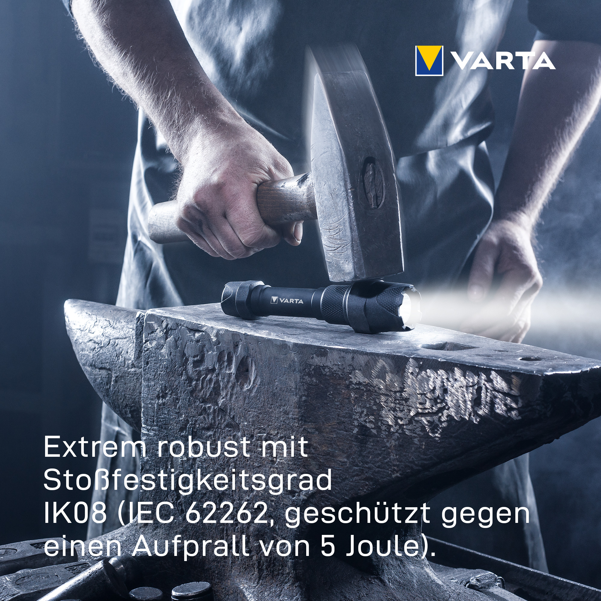 Eine Person schlägt mit einem Hammer auf eine robuste Varta-Taschenlampe auf einem Amboss.