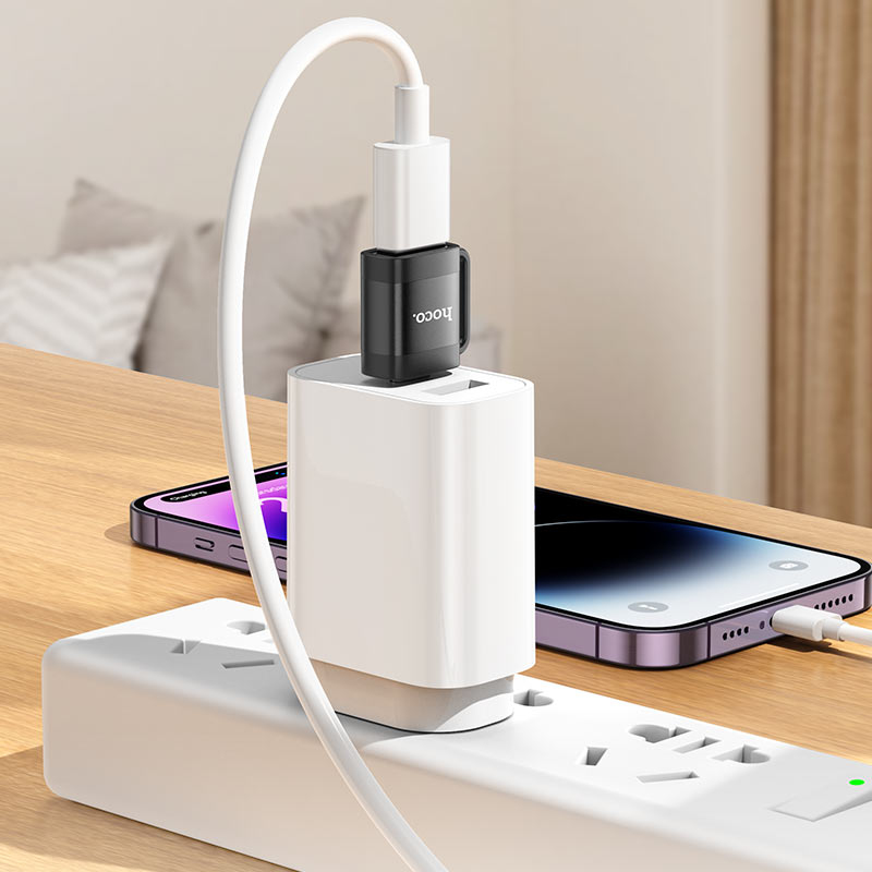 Ein weißes USB-Ladegerät mit schwarzem Adapter steckt in einer Steckdosenleiste auf einem Holztisch.