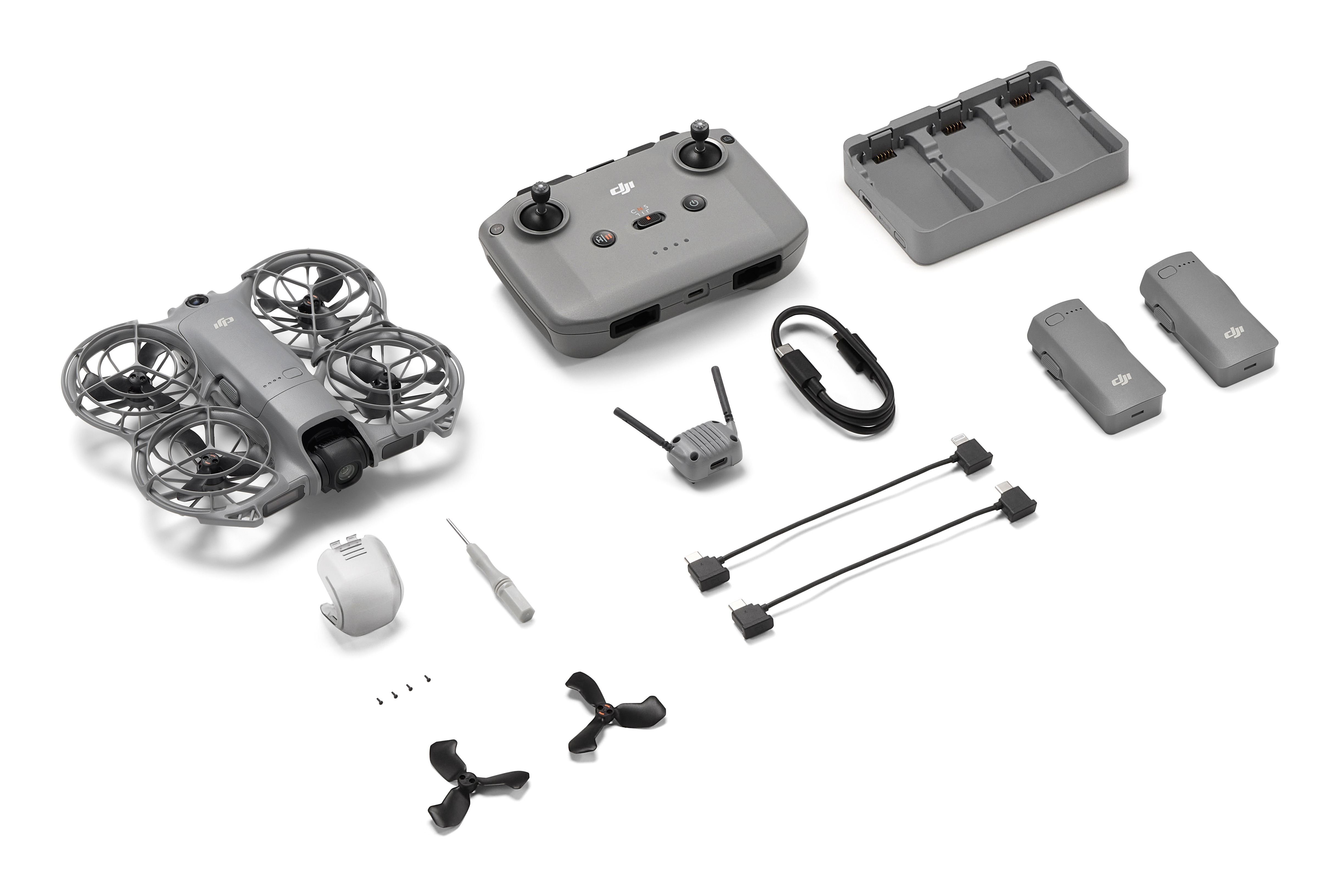 Un dron gris, control remoto, baterías, centro de carga, cables, herramientas y repuestos sobre fondo blanco.