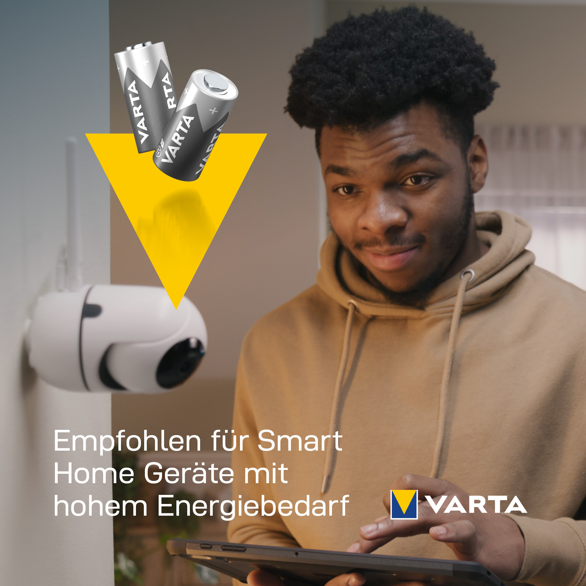 Un jeune homme sourit en installant une caméra de sécurité connectée avec des piles VARTA.