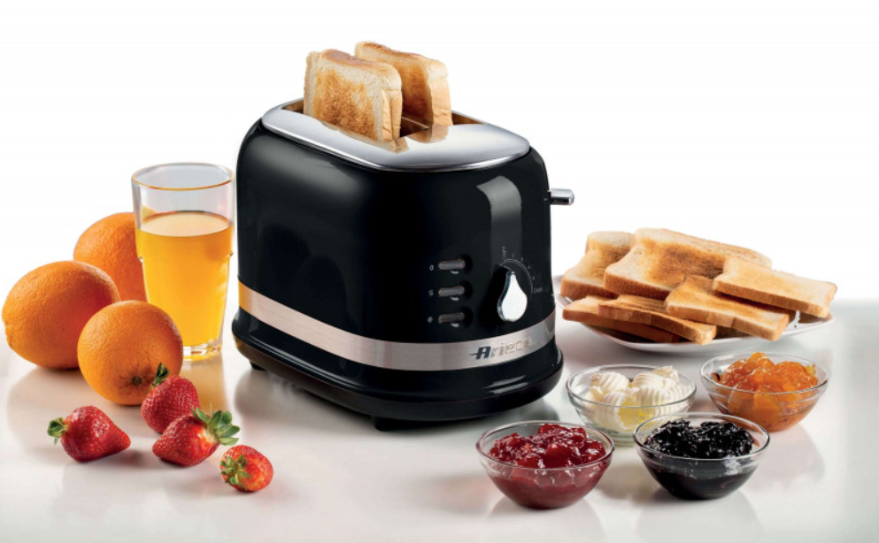 Ein schwarzer Toaster mit Toast, frischen Orangen, Saft, Erdbeeren und verschiedenen Aufstrichen auf einem Tisch.