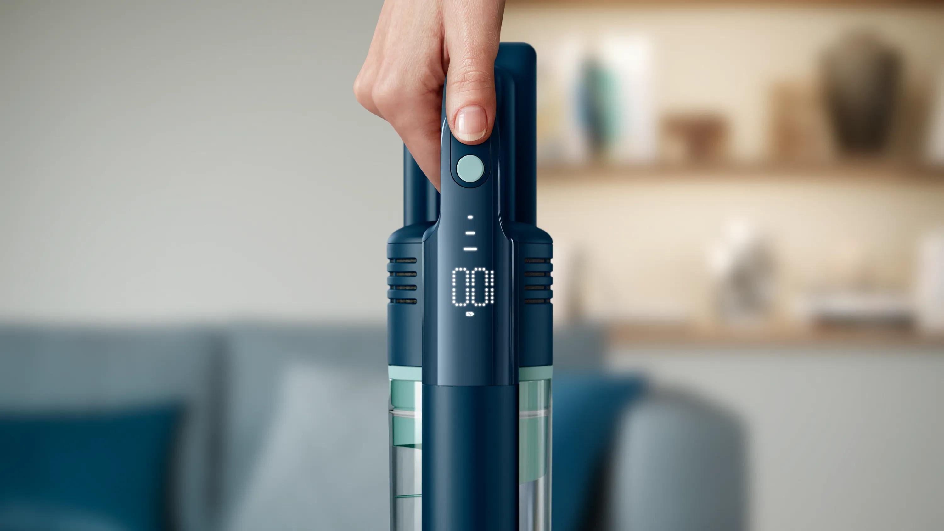 Hand houdt blauwe steelstofzuiger met digitaal display vast.