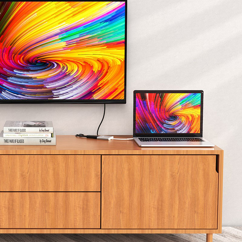 Ein Laptop und ein Fernseher auf einem Holzschrank zeigen bunte abstrakte Muster vor einer weißen Wand.