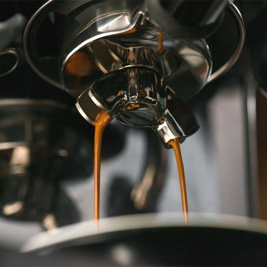 Espressosträhle fließen aus einem verchromten Siebträger in eine Tasse.