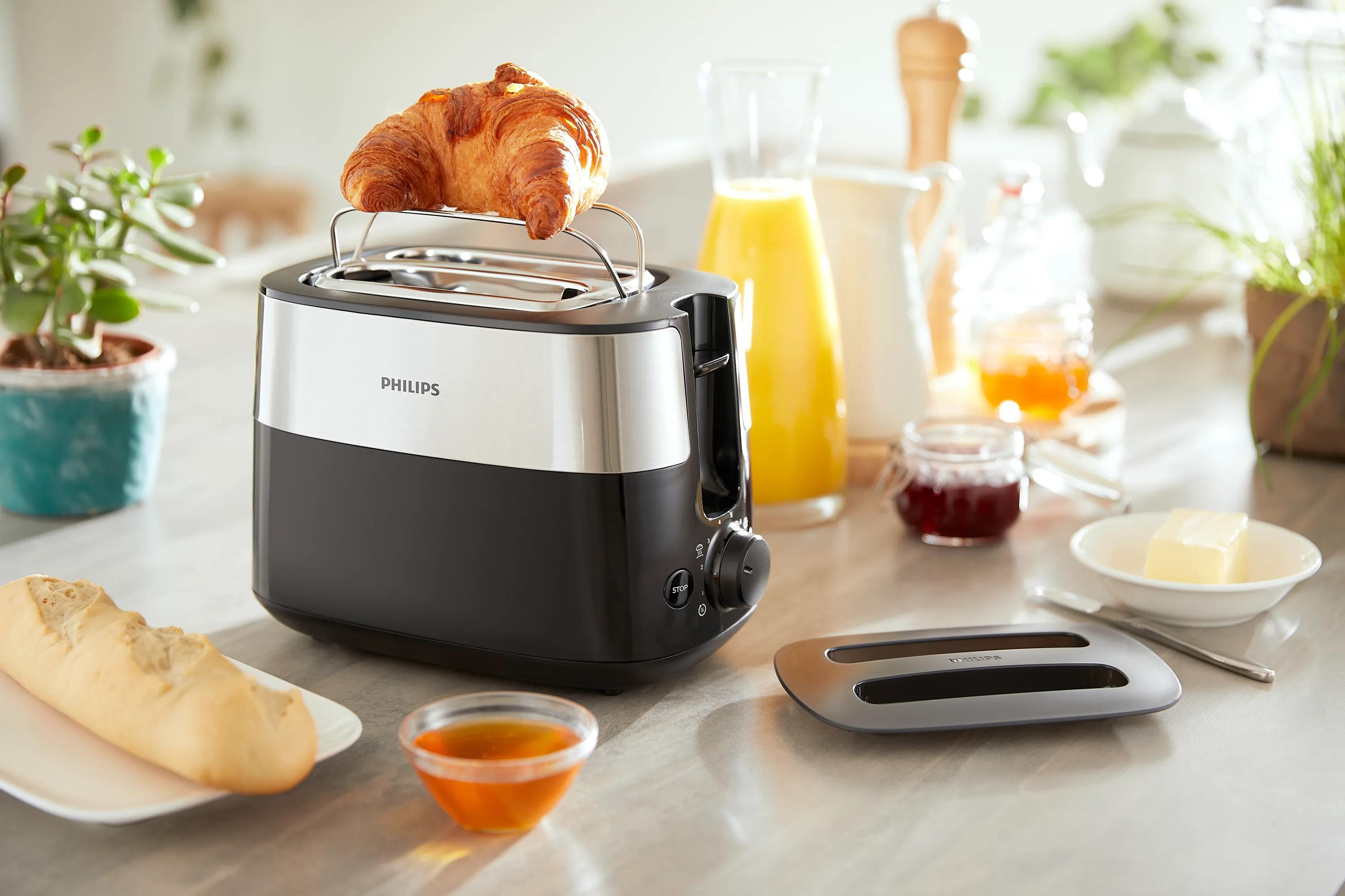 Un toaster Philips nero e argento con un croissant che si scalda sulla griglia superiore in una cucina luminosa.