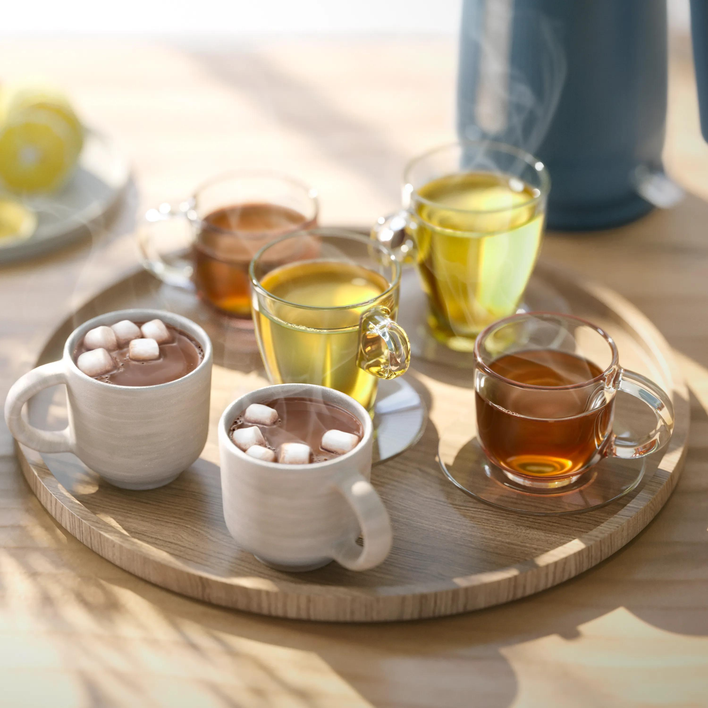 Een houten dienblad met warme dranken, waaronder bekers cacao met marshmallows en glaswerk met thee.