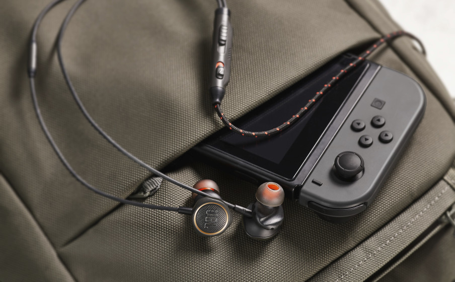 Una console di gioco e auricolari JBL nella tasca di uno zaino verde oliva.