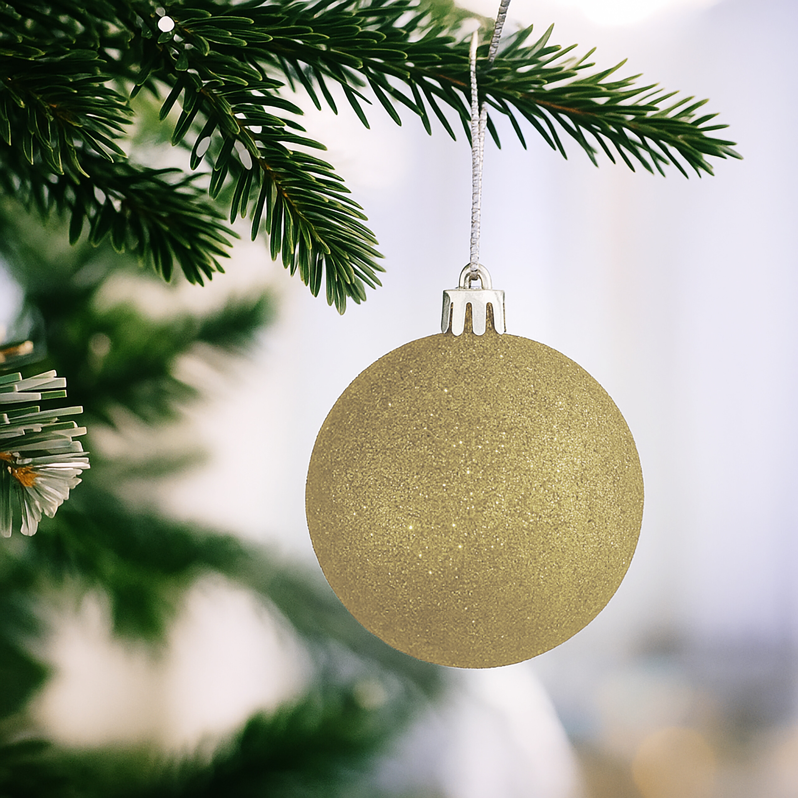 Eine glitzernde goldene Weihnachtskugel hängt an einem grünen Tannenzweig.