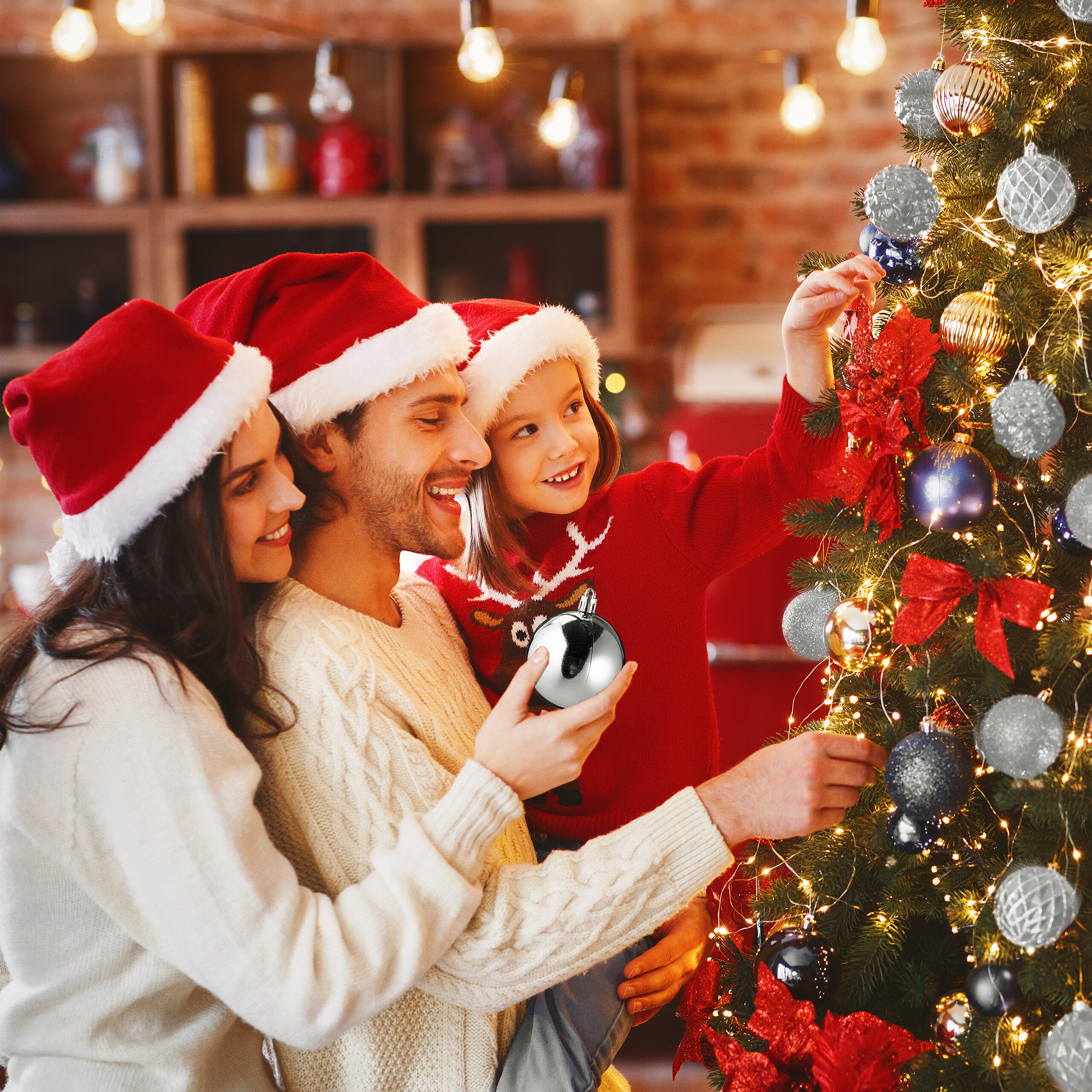 Eine Familie mit Weihnachtsmützen schmückt gemeinsam den Weihnachtsbaum.