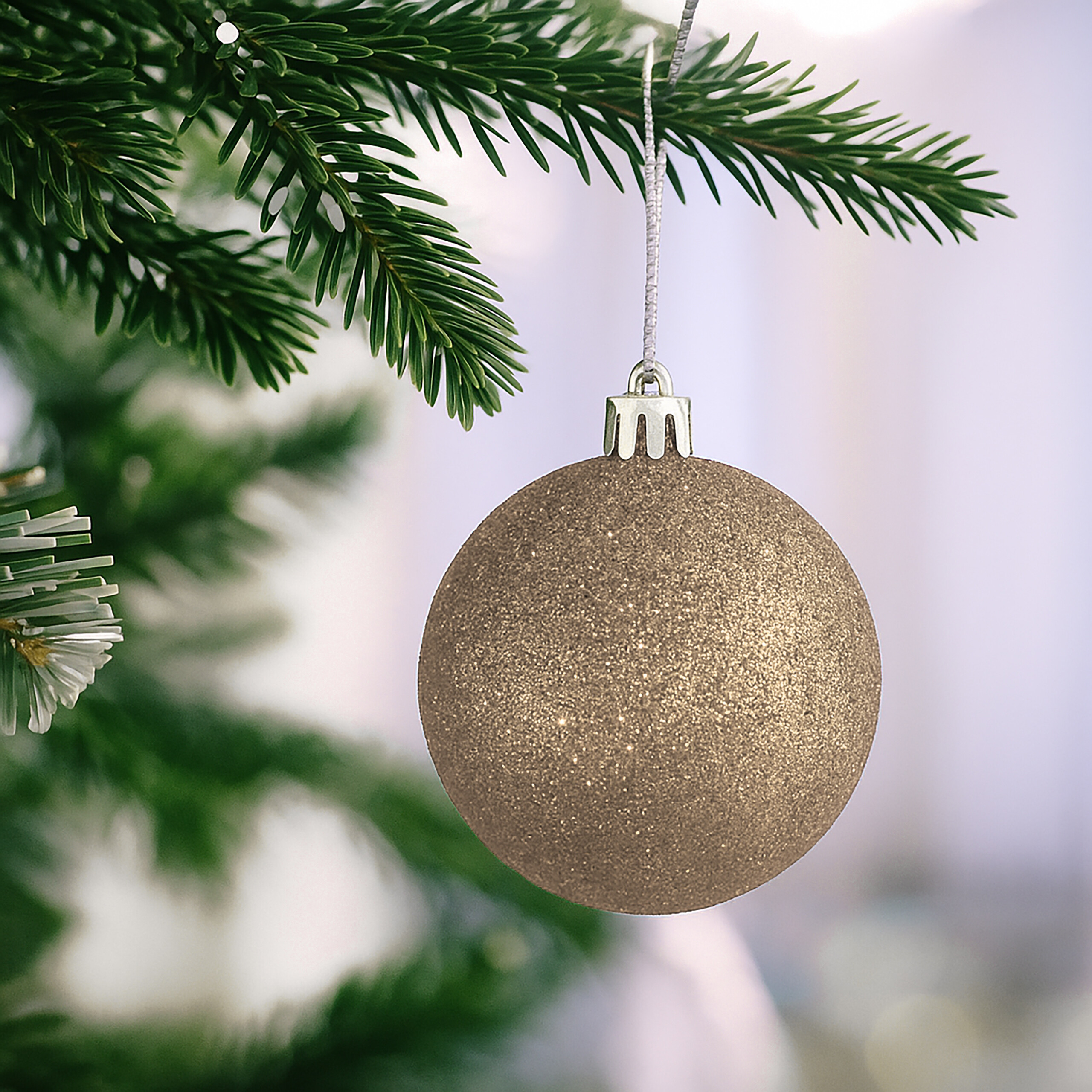 Eine glitzernde goldene Weihnachtskugel hängt an einem grünen Tannenbaum.