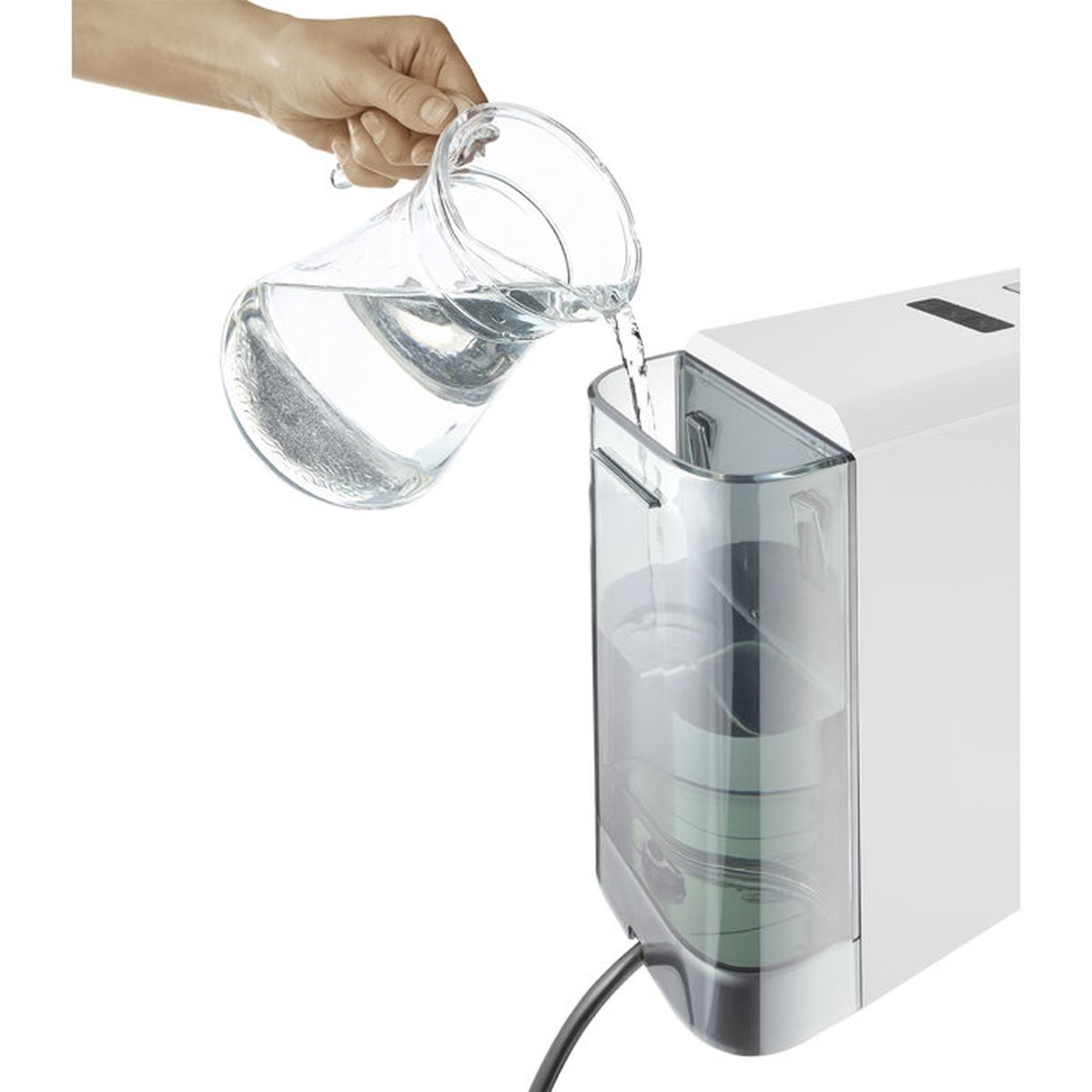 Una mano versa acqua da una caraffa di vetro nel serbatoio di un apparecchio bianco.