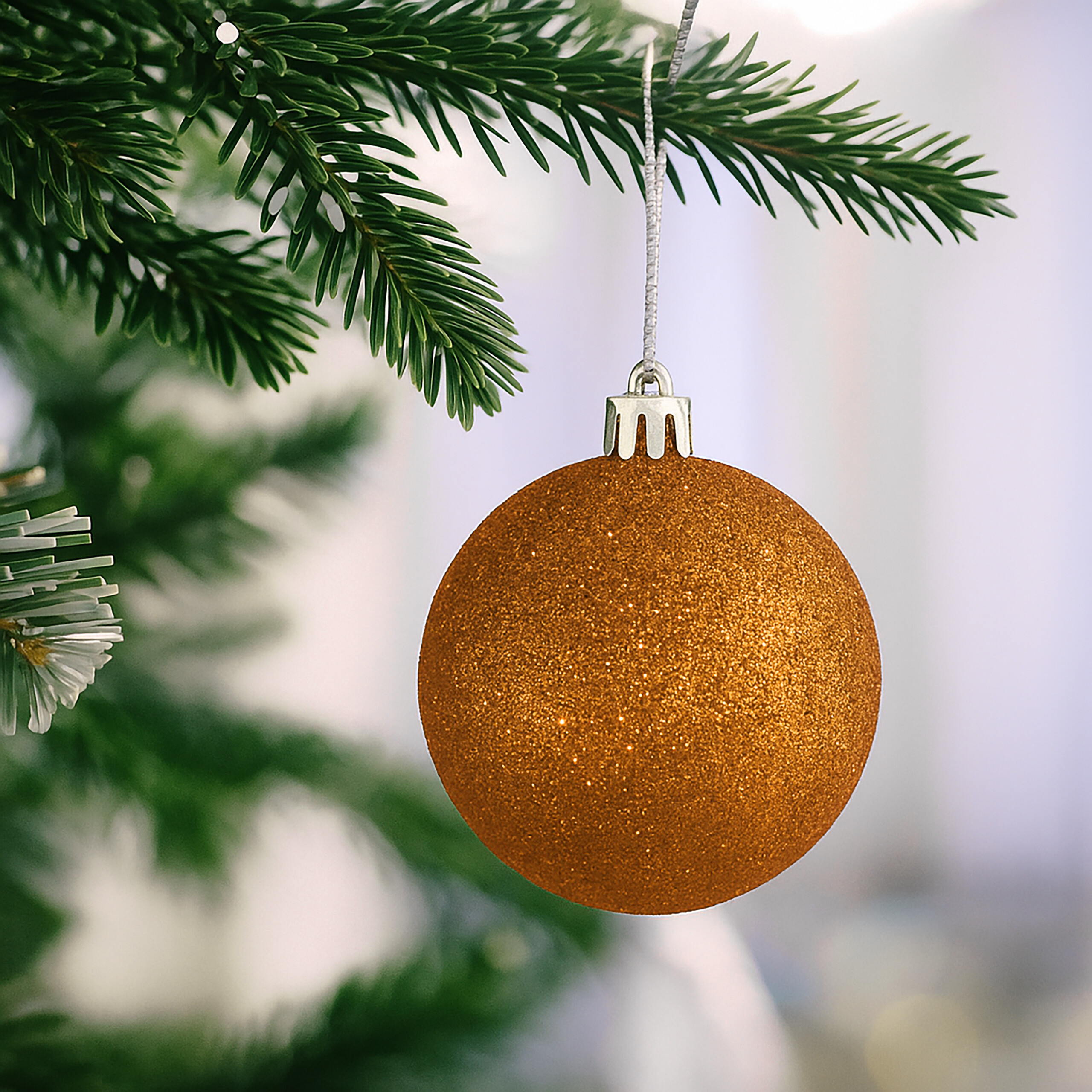 Eine glitzernde goldene Weihnachtskugel hängt an einem Tannenzweig.