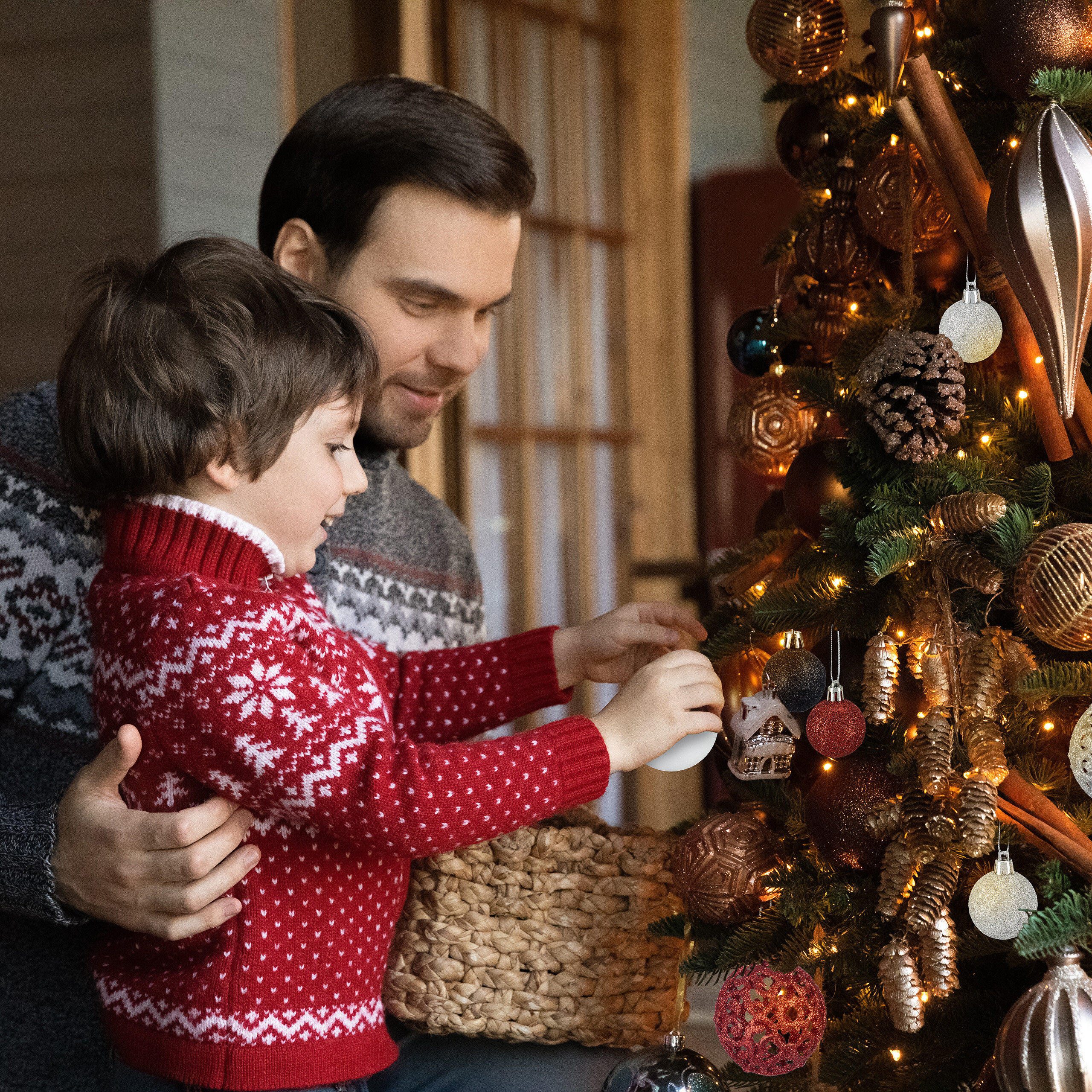 Ein Vater und sein Sohn schmücken zusammen einen hell erleuchteten Weihnachtsbaum.