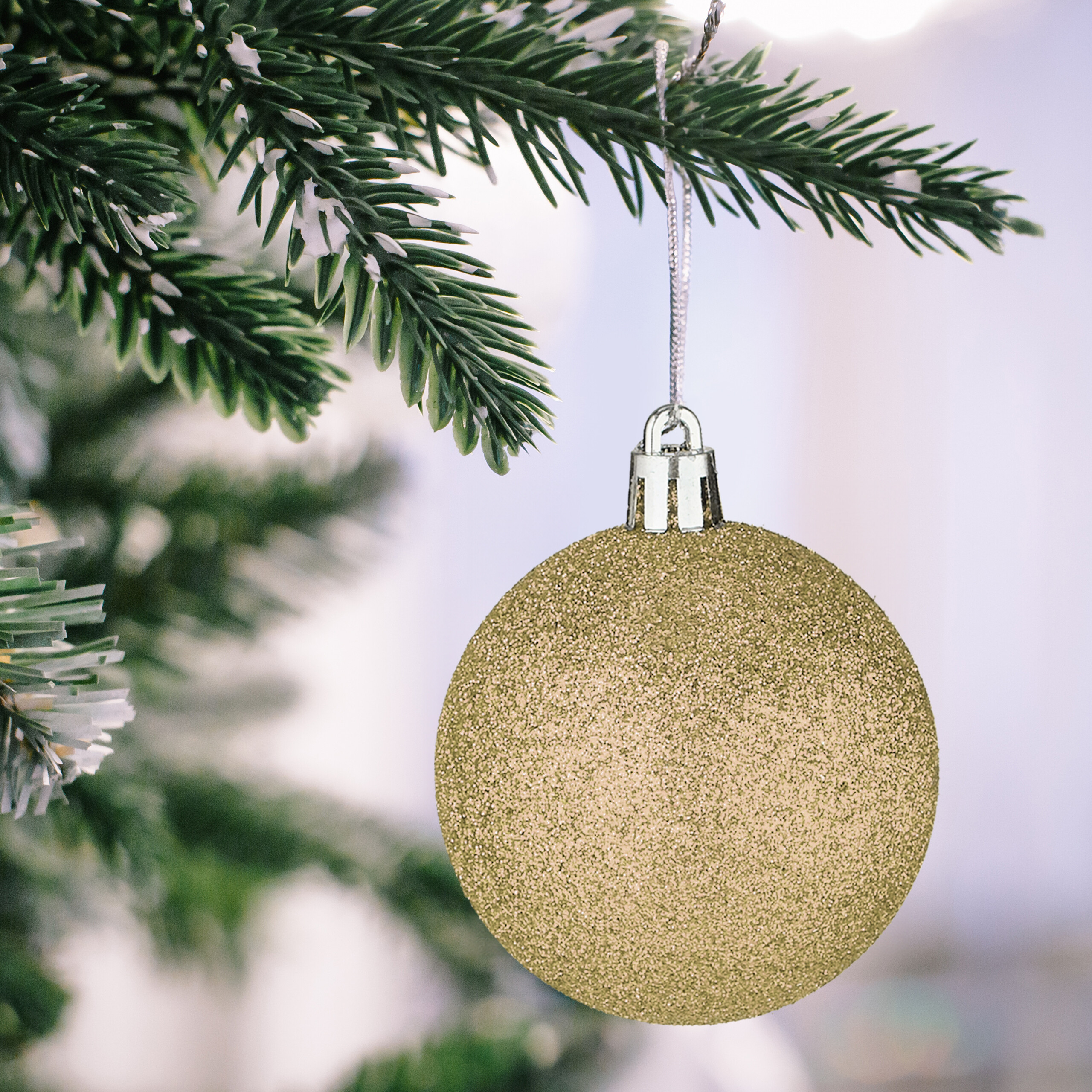 Eine glitzernde goldene Weihnachtskugel hängt an einem grünen Tannenzweig mit künstlichem Schnee.