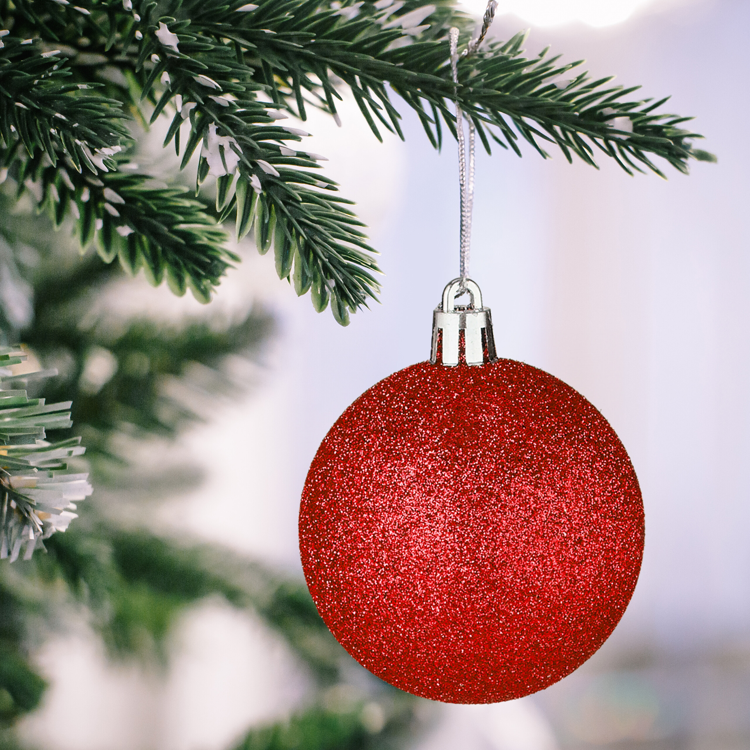 Eine glitzernde rote Christbaumkugel hängt an einem verschneiten Tannenast.