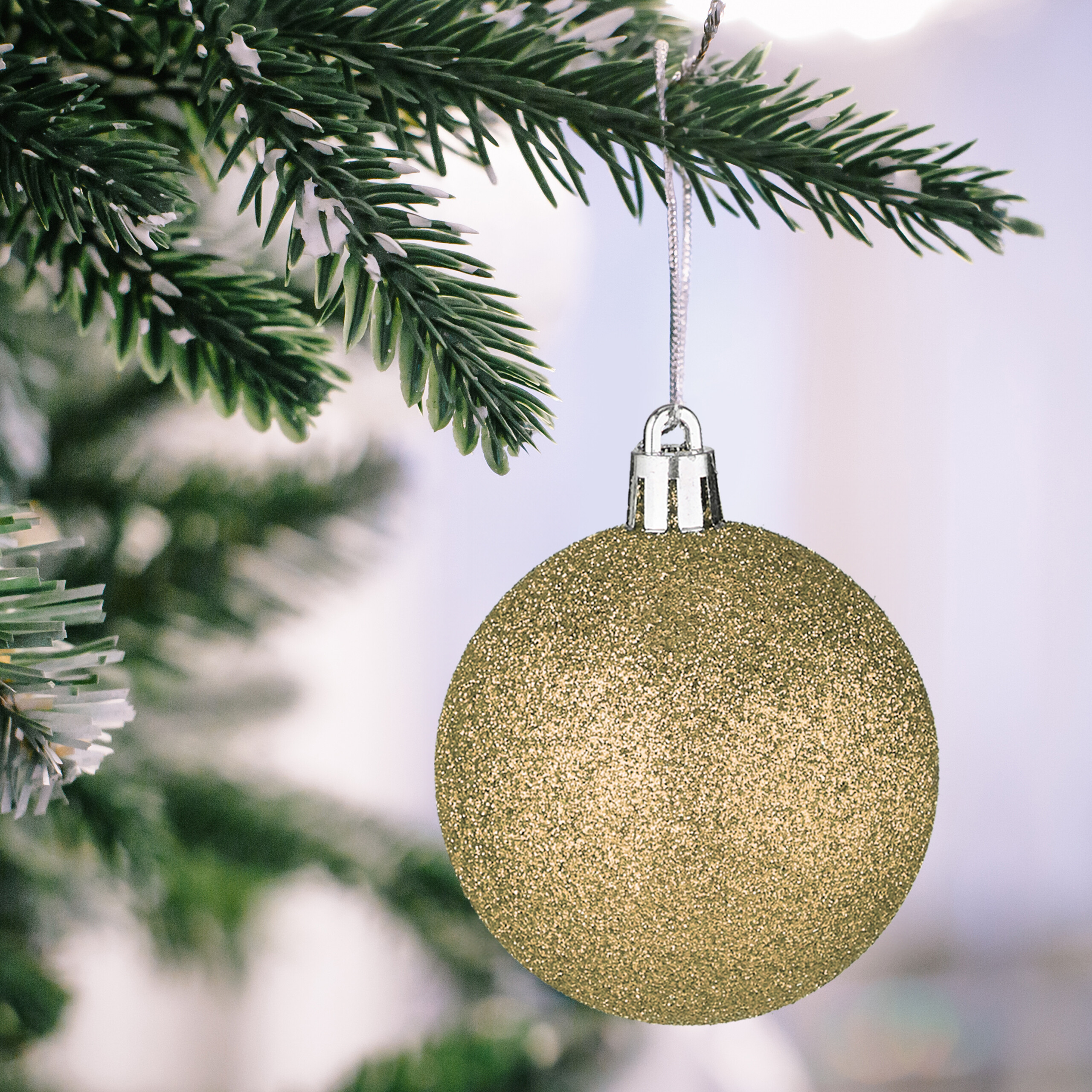 Eine glitzernde goldene Weihnachtskugel hängt an einem schneebedeckten Tannenzweig.