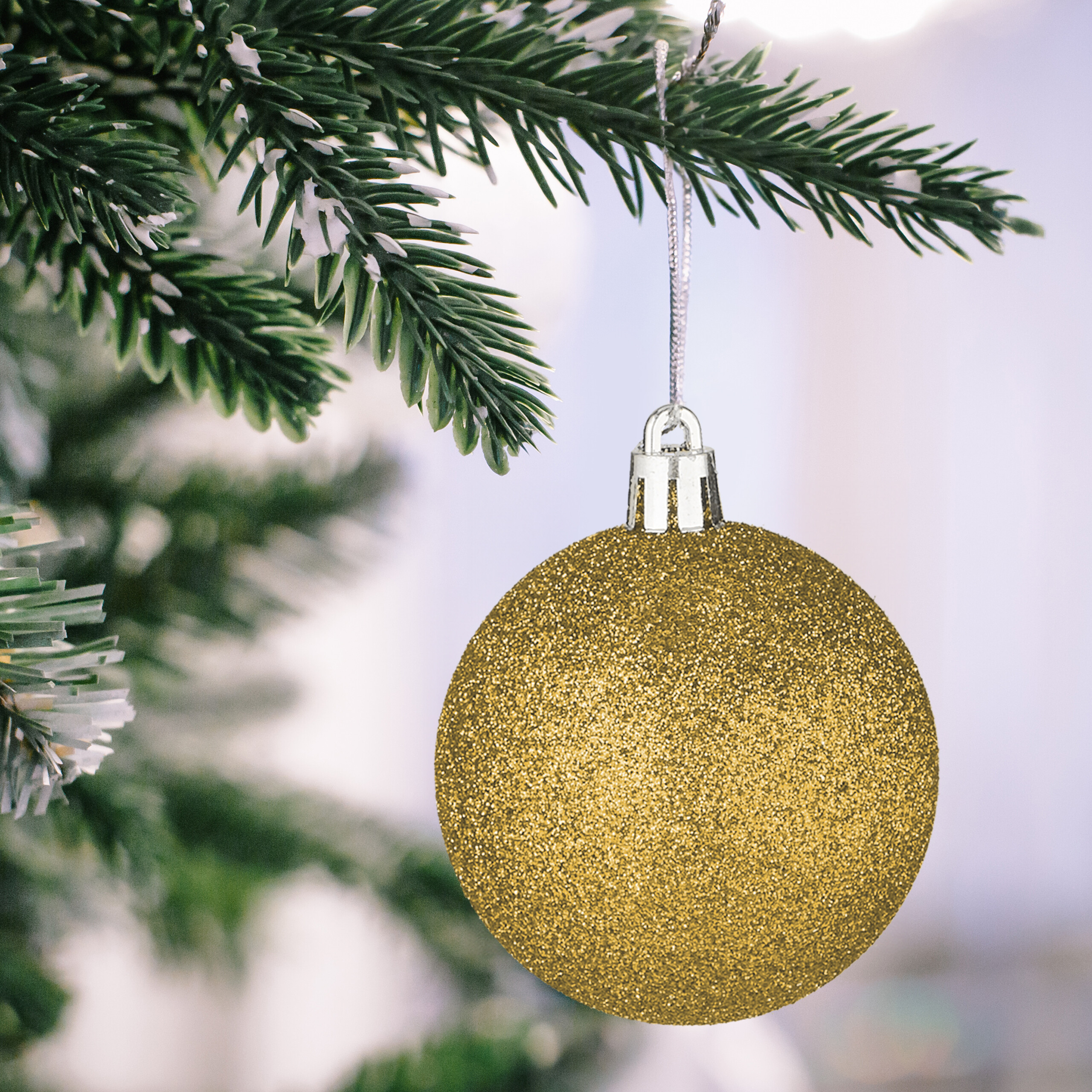 Eine glitzernde goldene Weihnachtskugel hängt an einem schneebedeckten Tonnenzweig.
