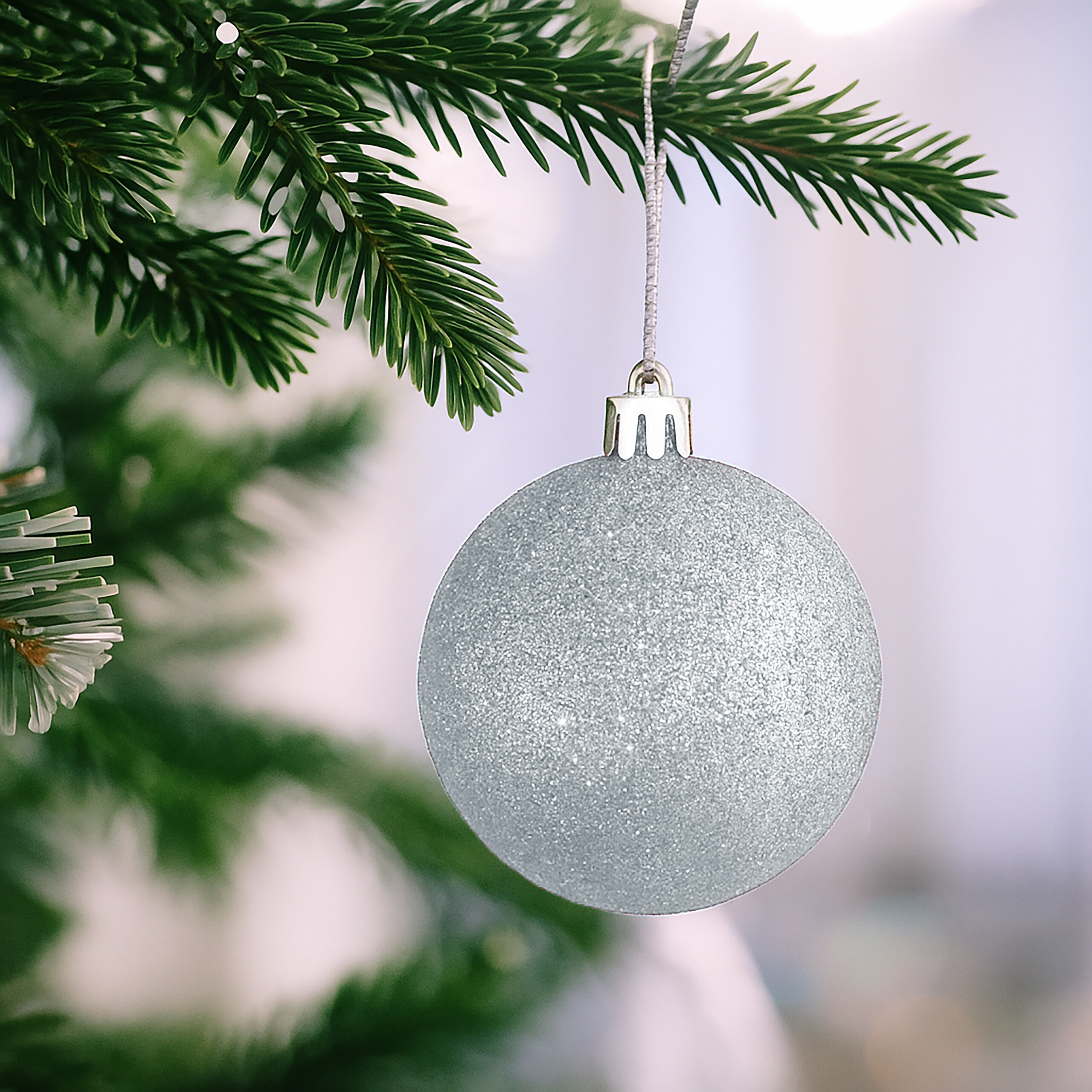 Eine glitzernde silberne Weihnachtskugel hängt an einem grünen Tannenbaum.