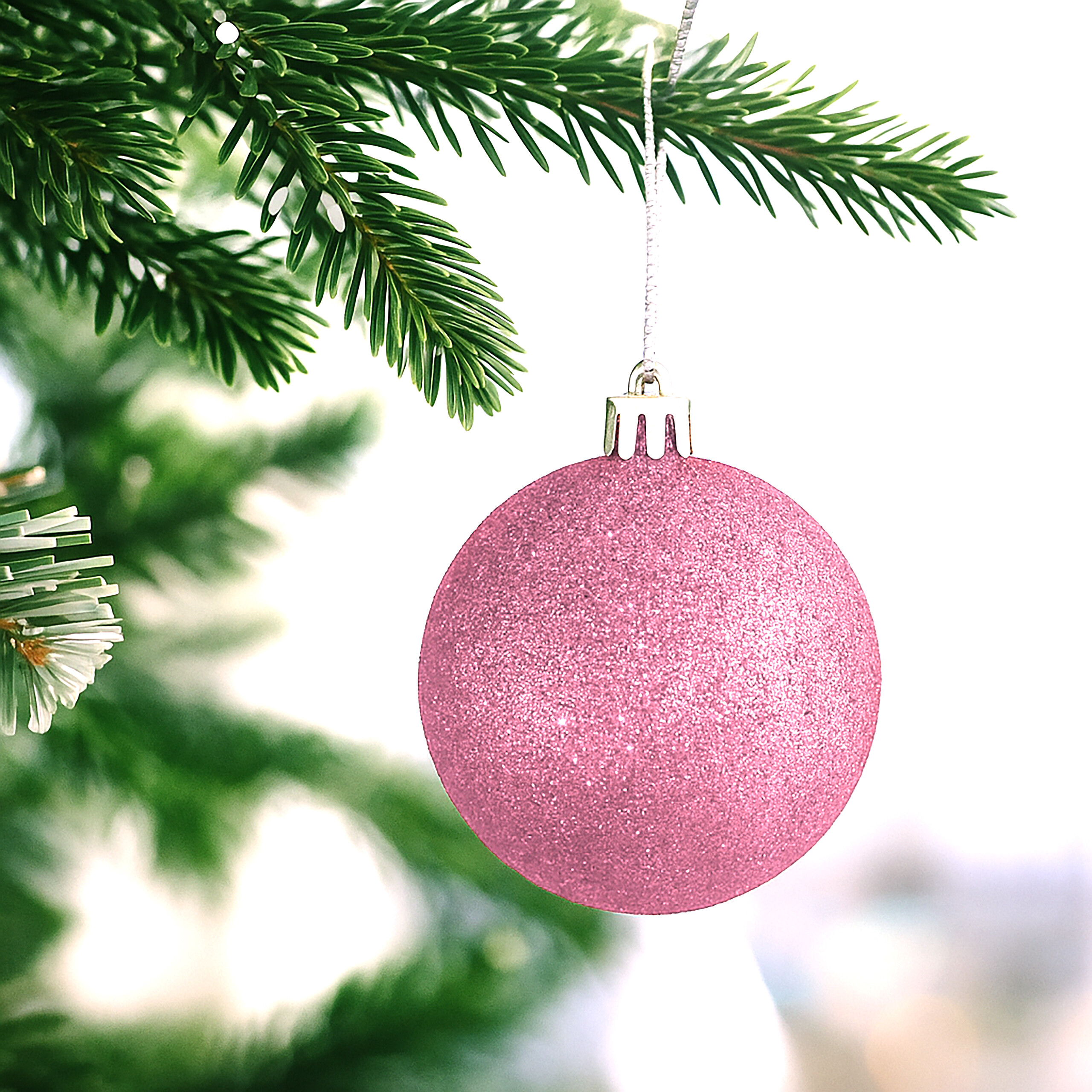 Eine glitzernde rosa Weihnachtskugel hängt an einem grünen Tannenbaumzweig vor hellem Hintergrund.