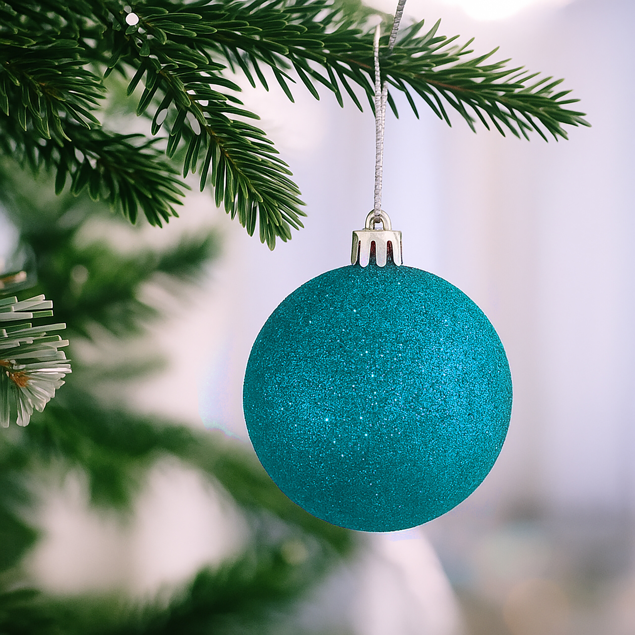Eine glitzernde türkise Weihnachtskugel hängt an einem grünen Tannenzweig.