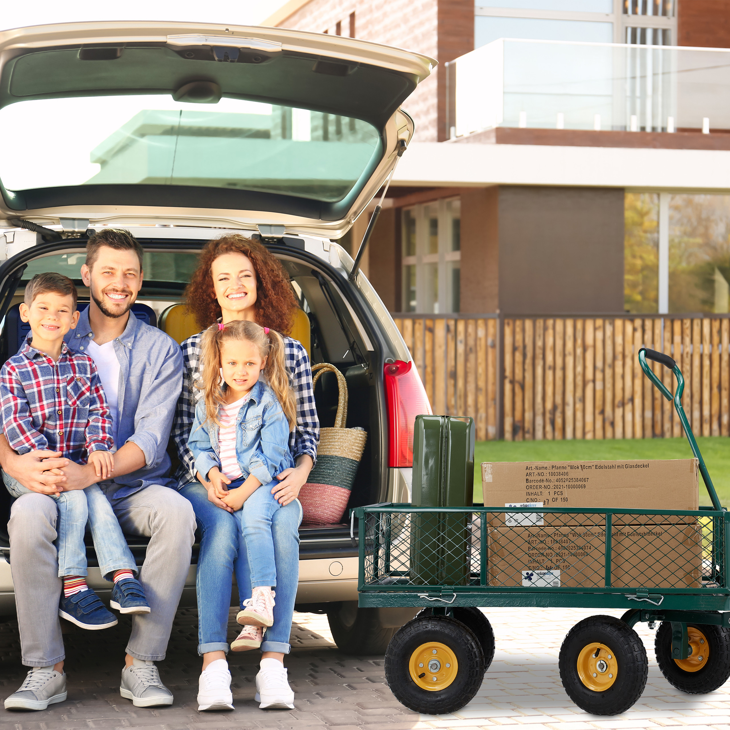 Eine glückliche vierköpfige Familie sitzt im offenen Kofferraum eines Autos neben einem grünen Bollerwagen.