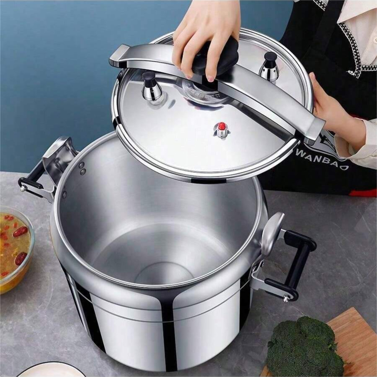Una persona abre la tapa de una olla a presión de acero inoxidable plateada grande en una encimera.