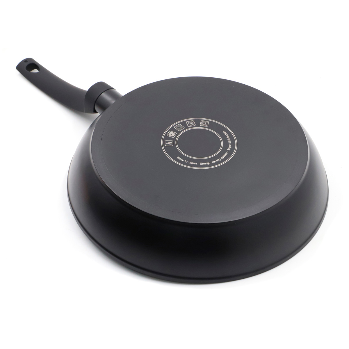 Una sartén negra está boca abajo sobre una superficie blanca, mostrando su base con diseño circular y mango.