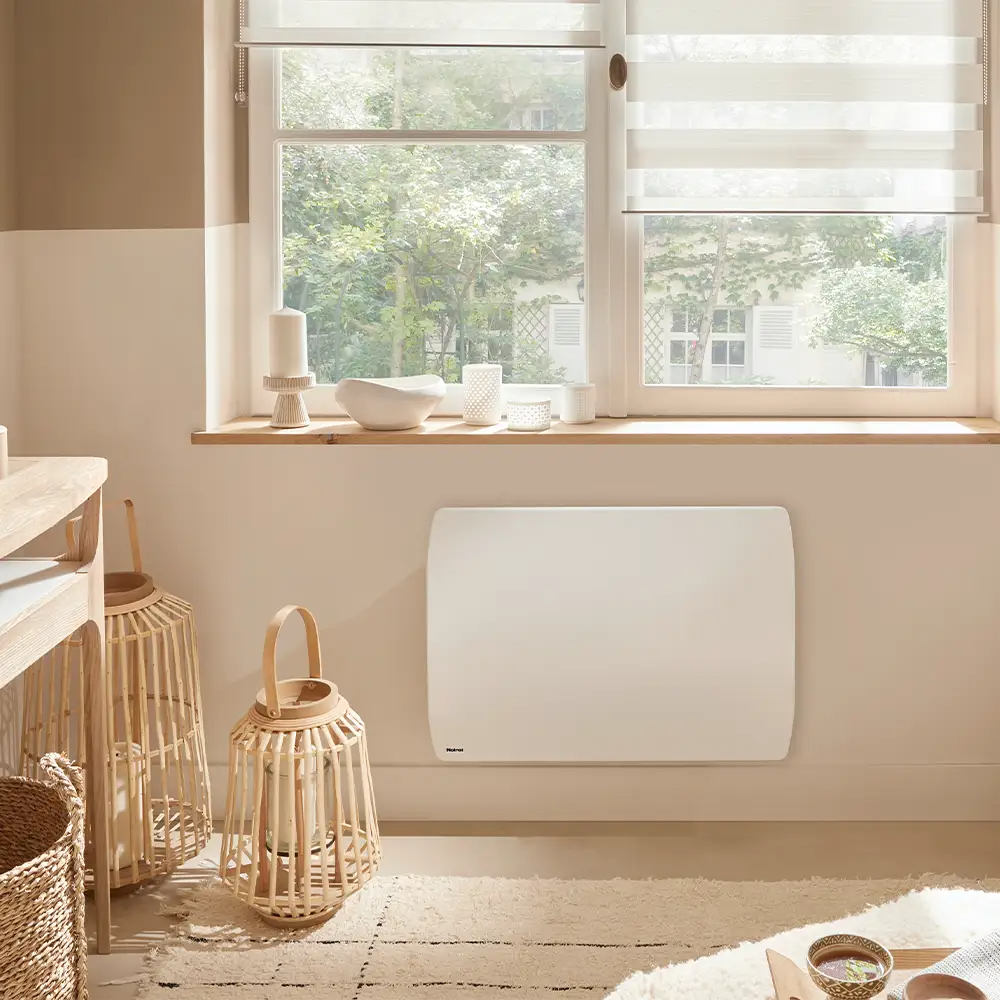 Wohnzimmer mit weißem Wandheizkörper unter dem Fenster, Holzlaternen und grünem Ausblick.