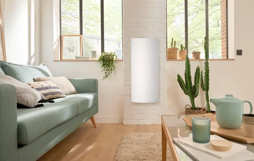 Wohnzimmer mit mintgrünem Sofa, weißem Heizkörper an der Ziegelwand, Pflanzen und Holztisch.