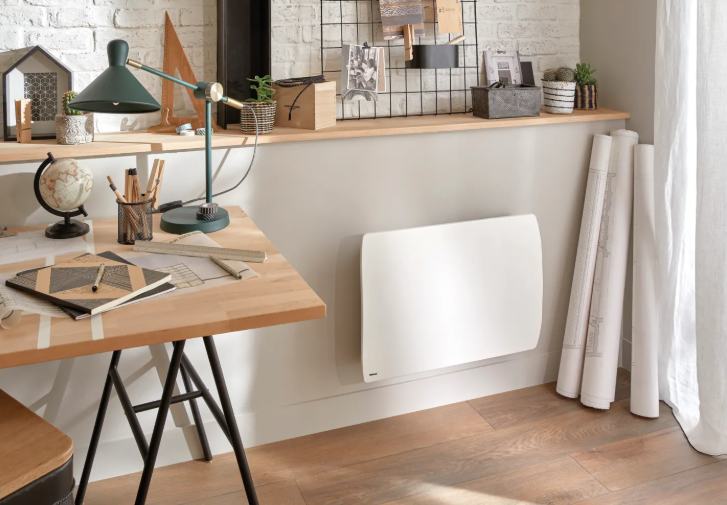 Ein weißer Heizkörper an einer Wand in einem modernen Arbeitszimmer mit Holztisch und Dekoration.