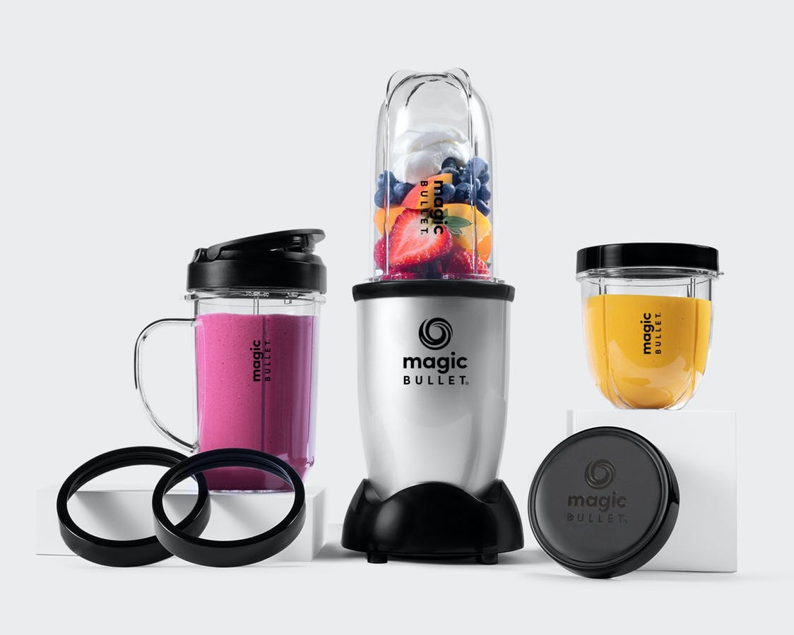 Magic Bullet blender with a cup of fruit, a pink smoothie mug, a small yellow cup, and two black lip rings.
