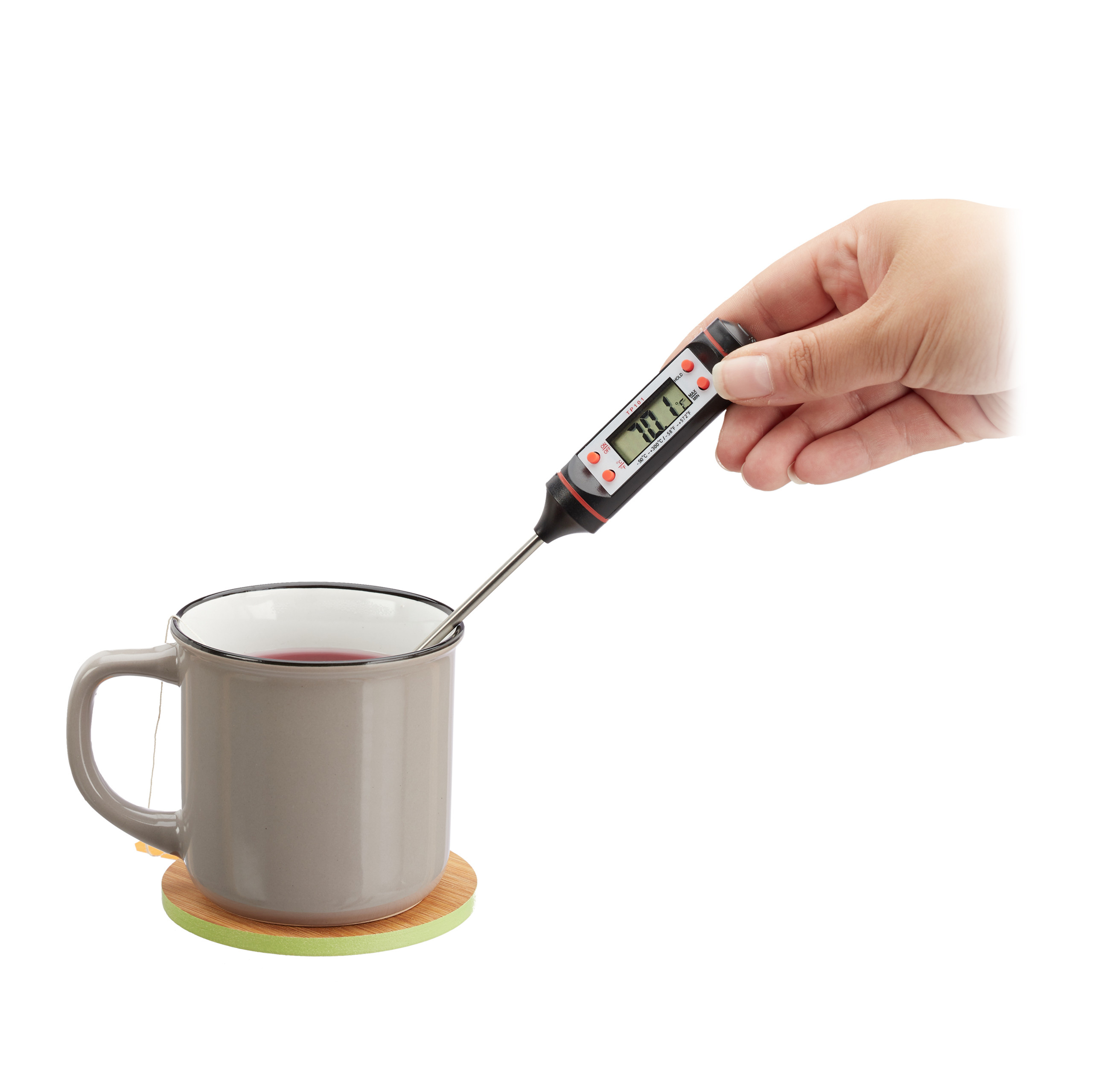 Eine Hand misst mit einem Digitalthermometer die Temperatur von Tee in einer grauen Tasse auf einem Holzuntersetzer.