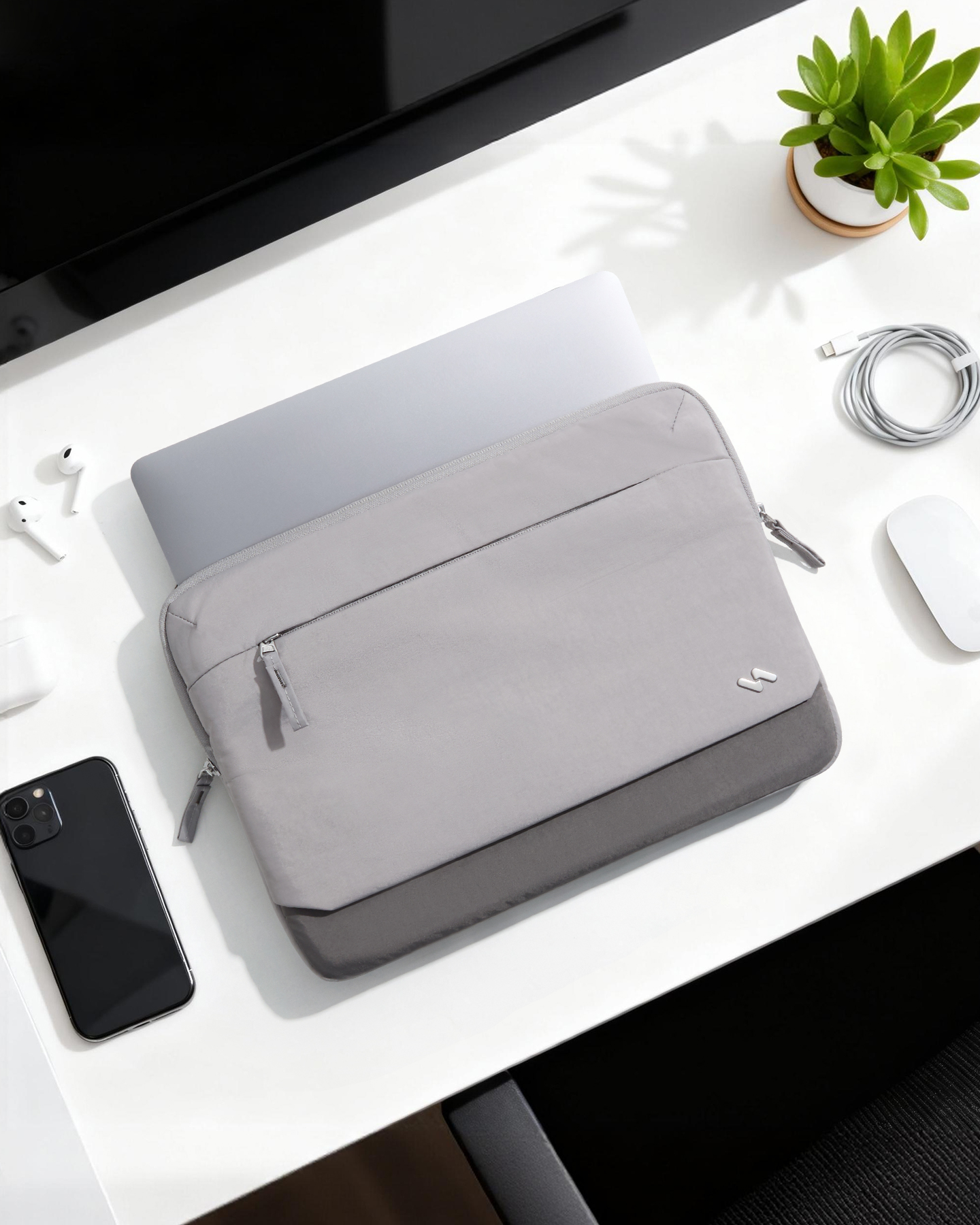Laptop in einer grauen Hülle auf einem weißen Schreibtisch mit Smartphone, Maus und einer kleinen Pflanze.