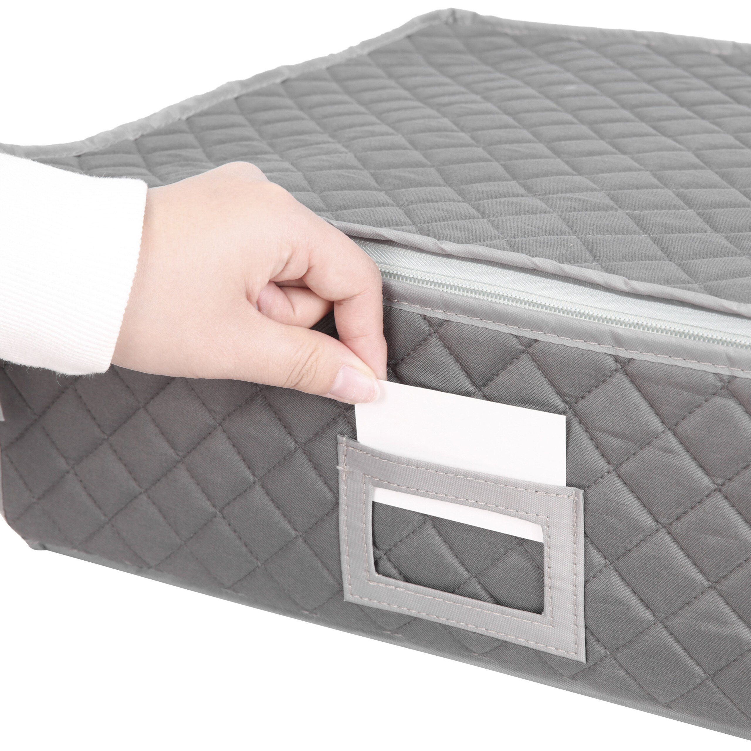 Eine Hand schiebt ein Namensschild in die transparente Tasche einer grauen, gesteppten Aufbewahrungsbox.