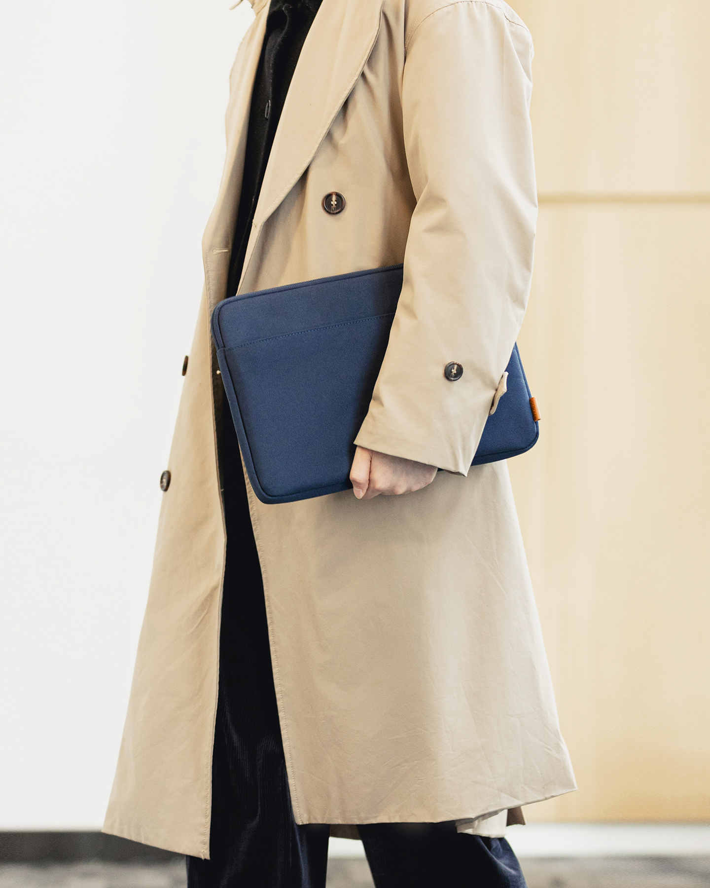 Eine Person im hellen Trenchcoat hält eine blaue Laptoptasche.